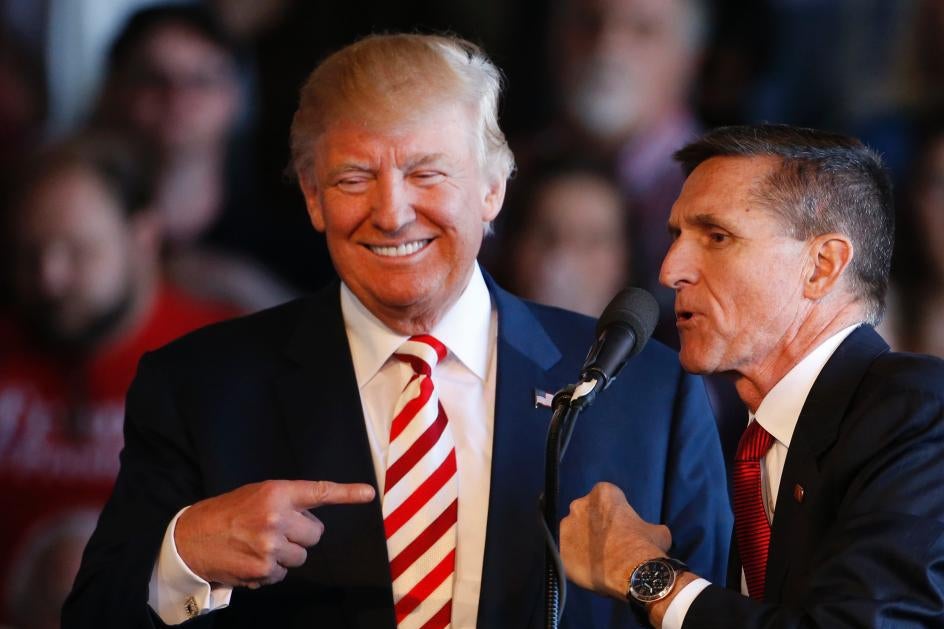 Michael Flynn leans toward Donald Trump to speak into a microphone.