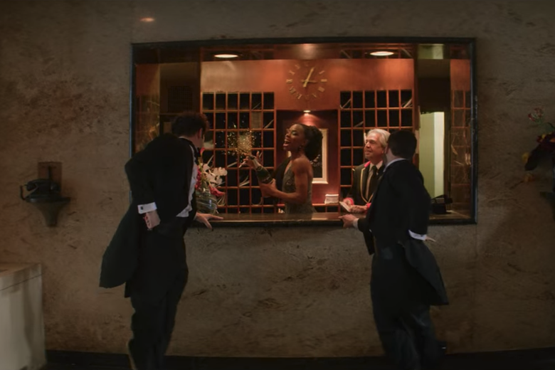 Andrew Garfield and Robin de Jesus dance in coats and tails in front of a concierge window where Luis Miranda, Jr. plays a concierge.