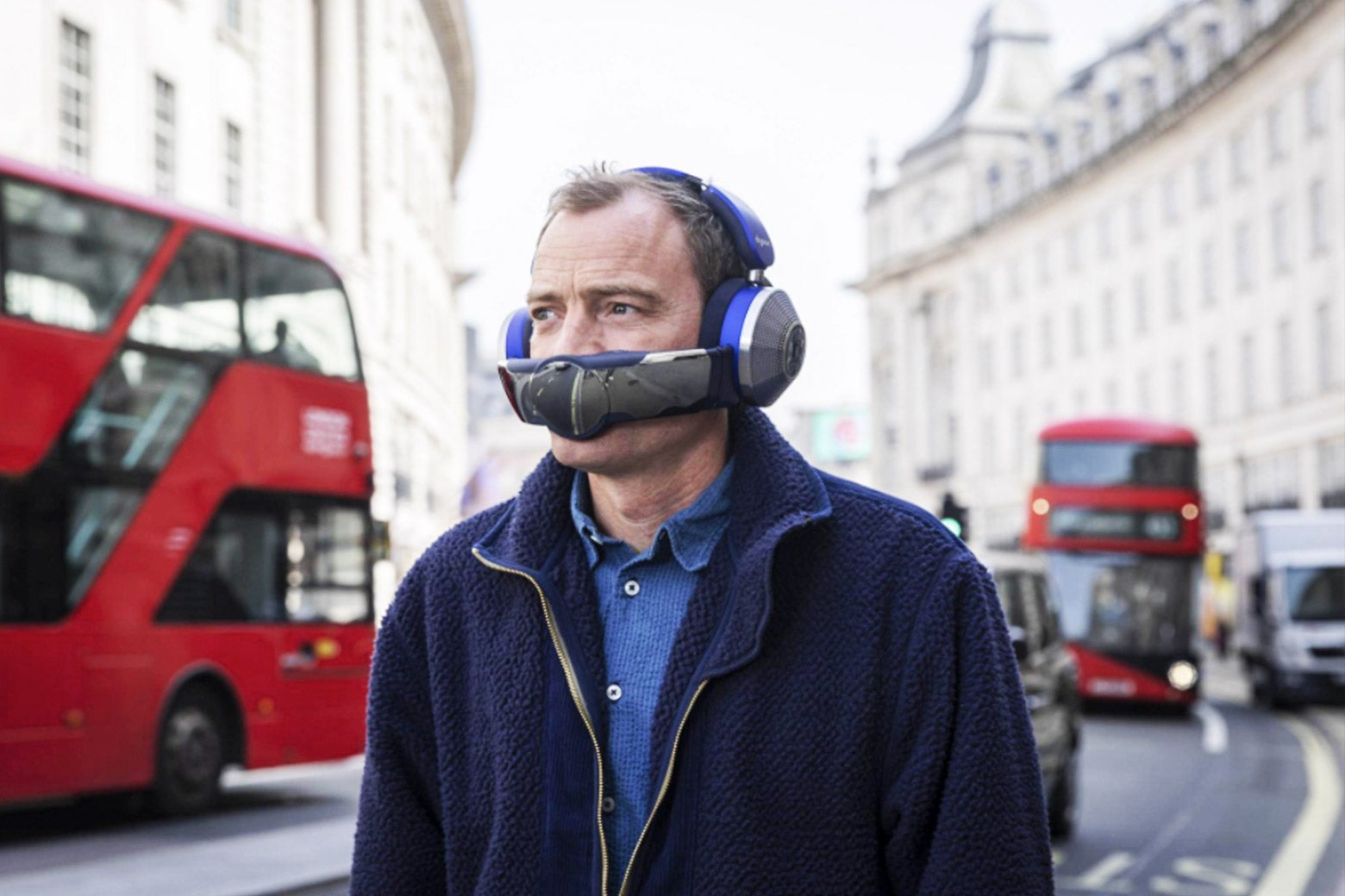 A man wearing the Dyson Zone, which looks like a pair of purple and silver headphones with a part that covers the mouth like the guys from Daft Punk, but less avant-garde and more like a mistake.