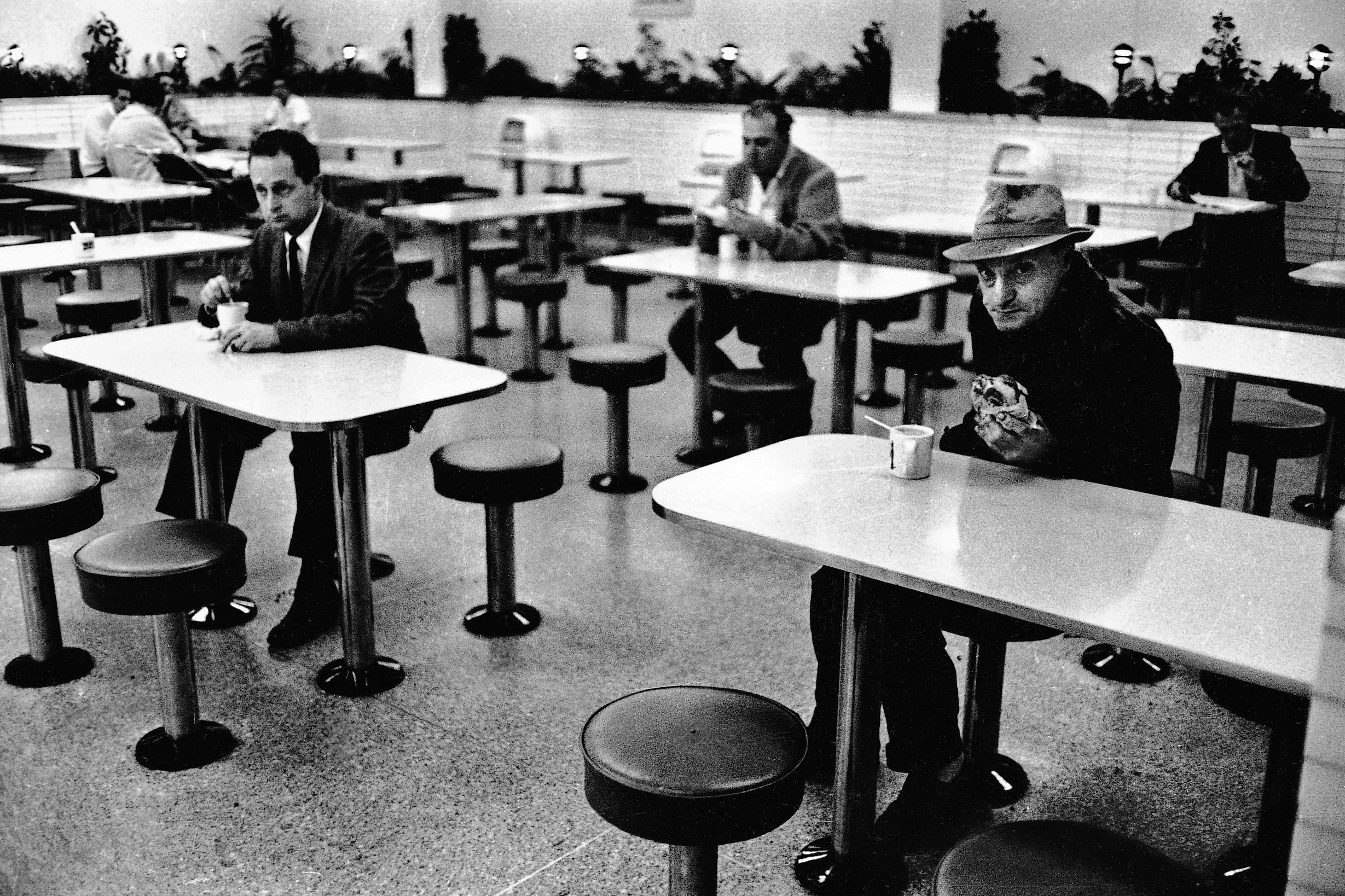 Several men sitting alone at tables inside a restaurant.