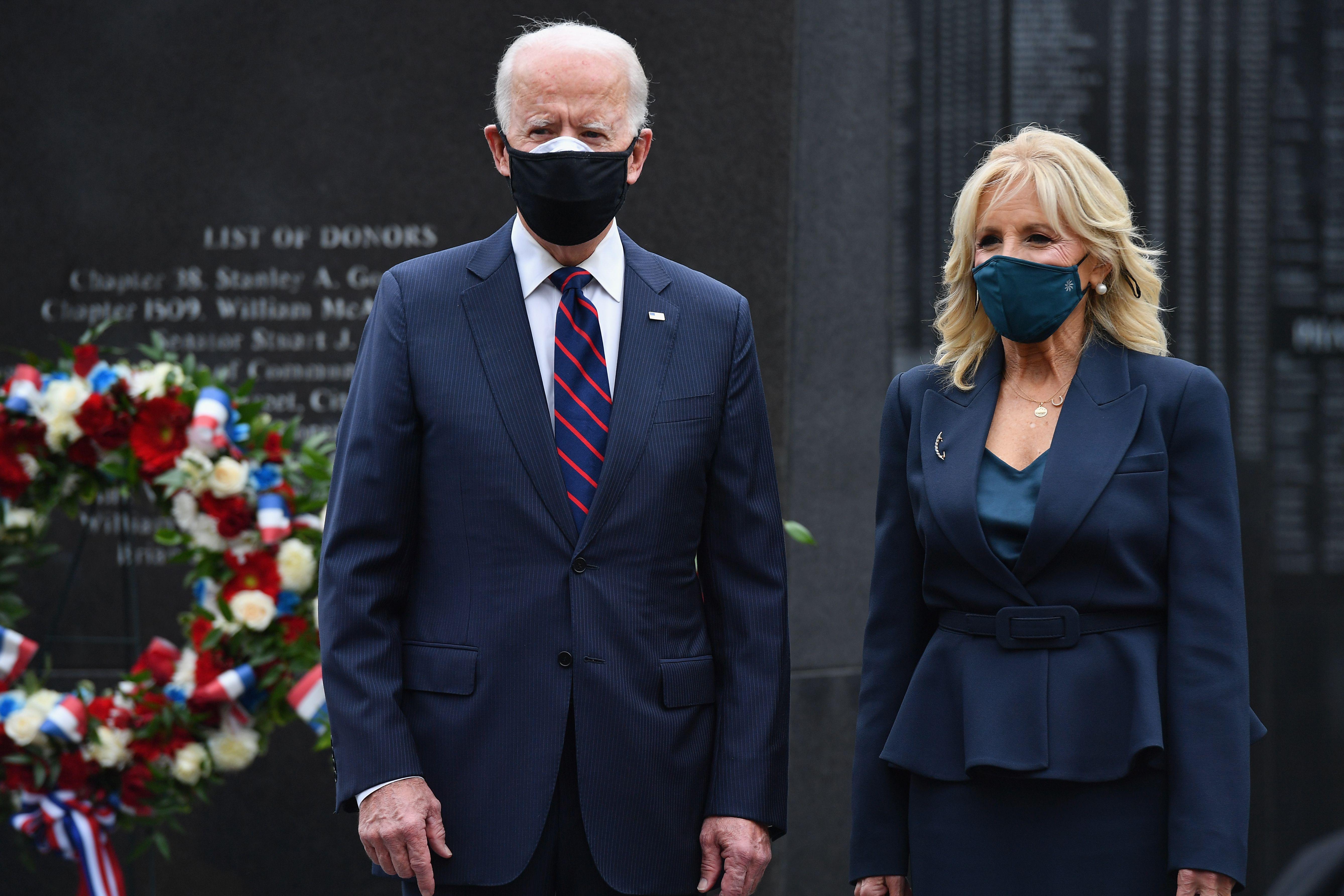 The pair wear black masks in front of a stone memorial.