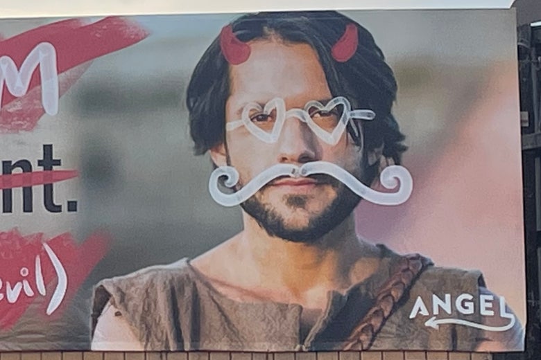 Billboard of a man dressed as Jesus lightly defaced with a white spray paint mustache, glasses, and devil horns.