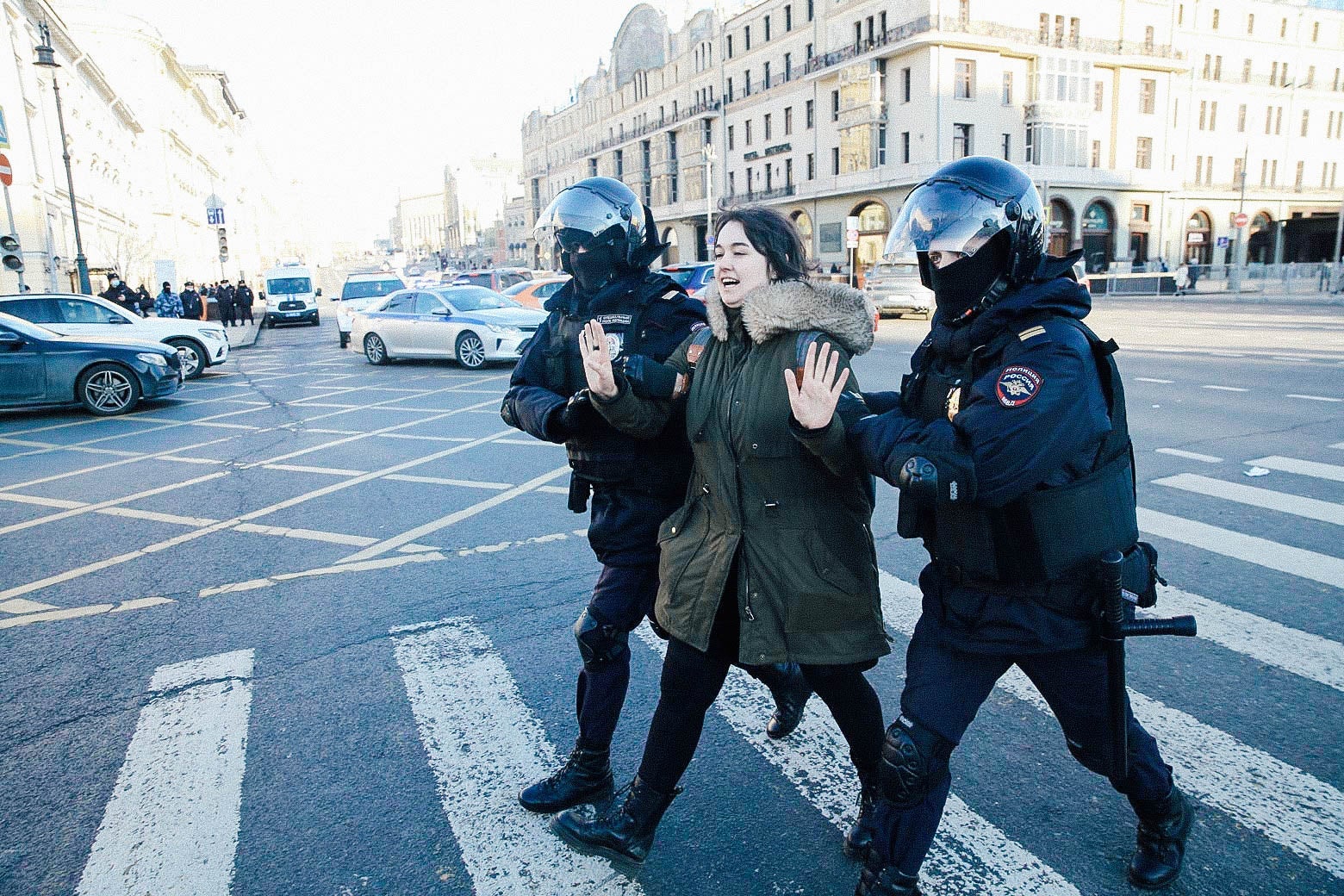 A woman holds up her hands as two police officers in riot gear walk her away.