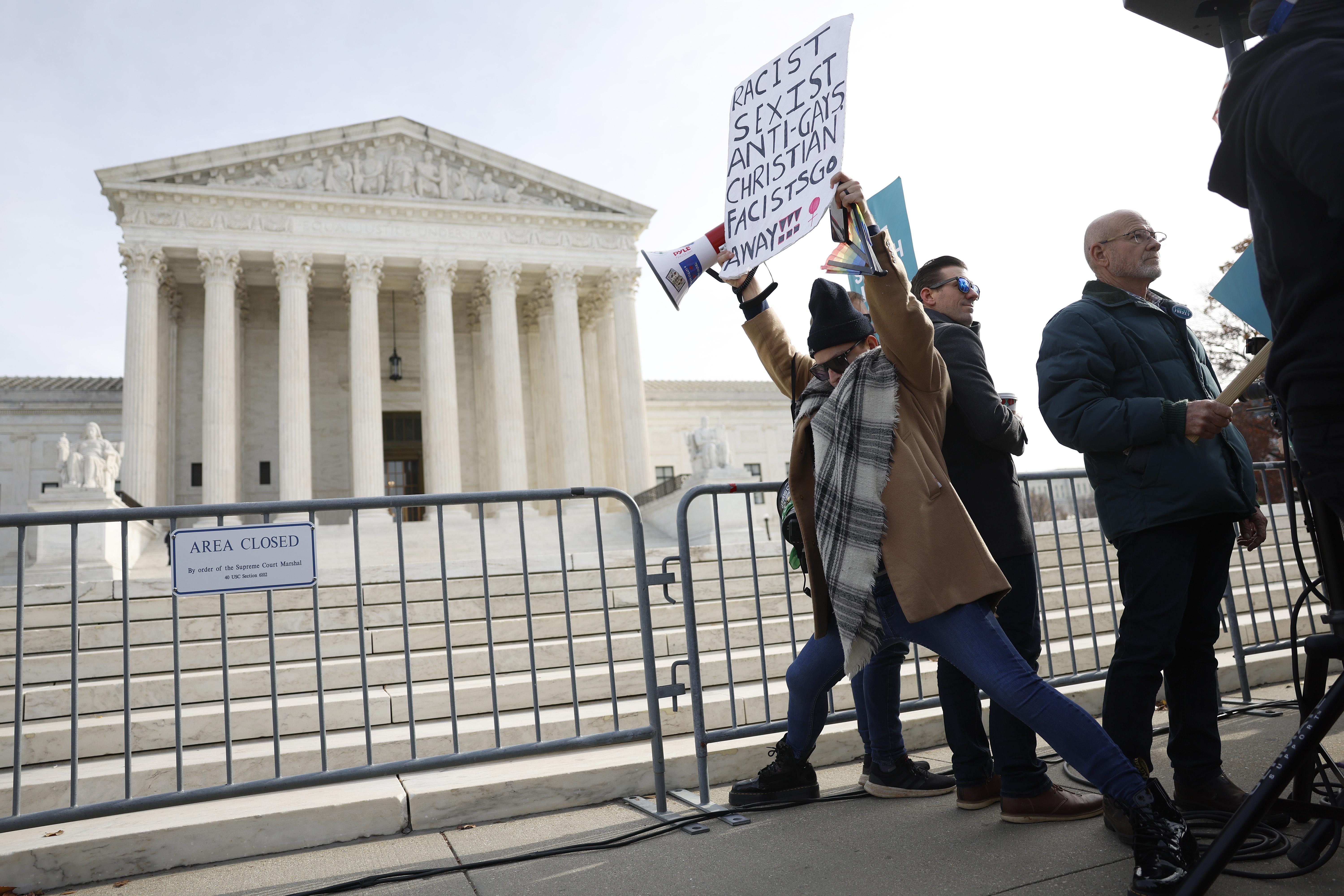 Protestors outside the Supreme Court — the Court building is seen at an angle, behind a fence. 