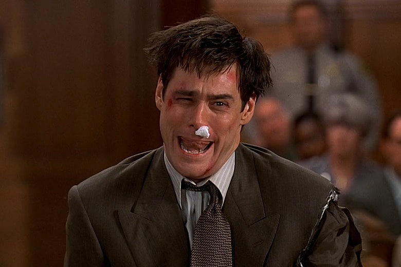 Jim Carrey faces the camera in a courtroom with a torn suit jacket, askew tie, piece of cotton in his nose, blood and bruises on his face, and mussed hair. He stands with his mouth open. 