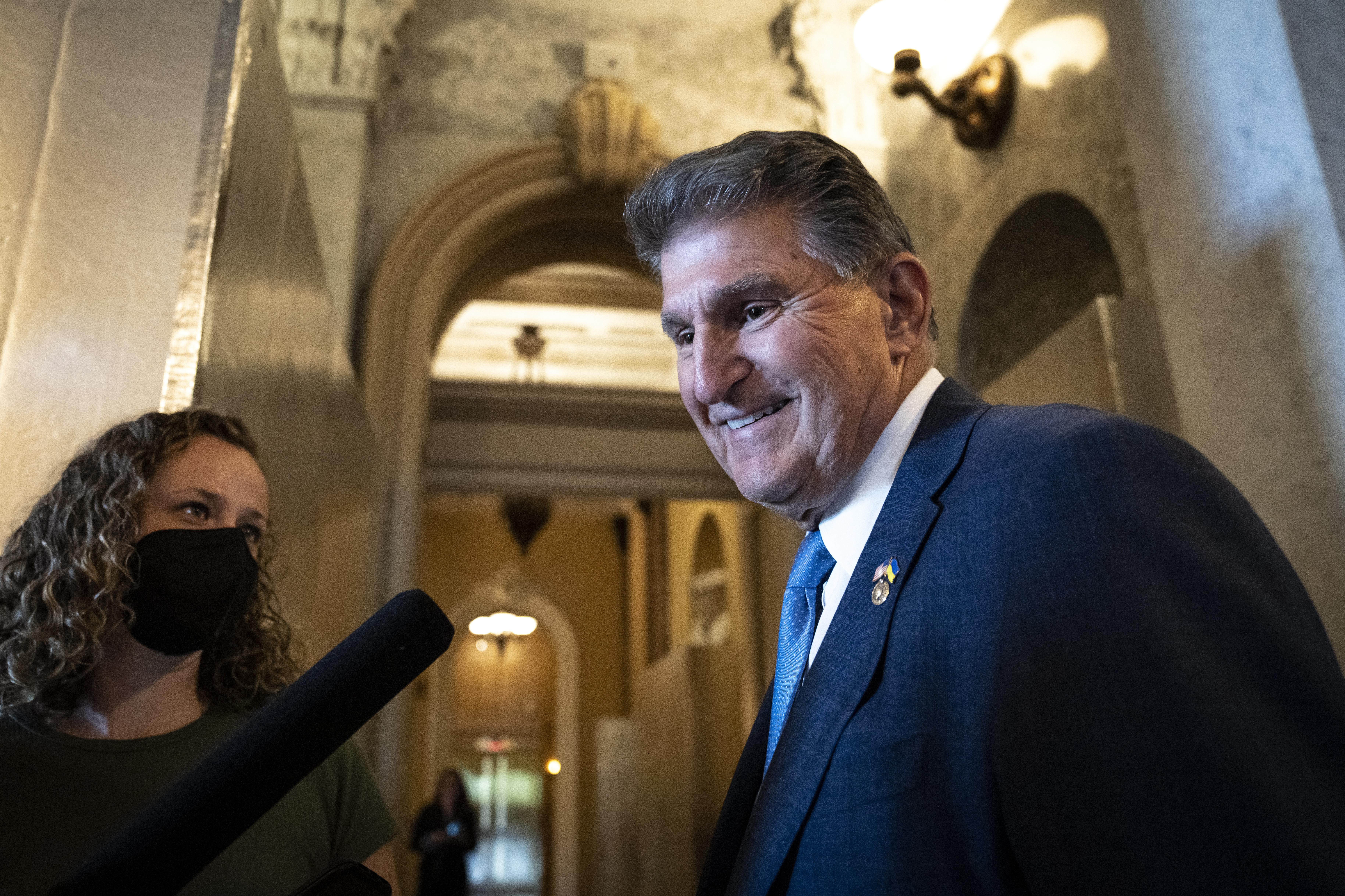 Joe Manchin smiles as a masked reporter with a microphone stands beside him.