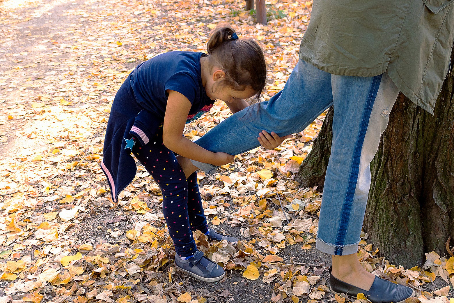 A small girl pulling her mother's leg during an autumn day at the park.