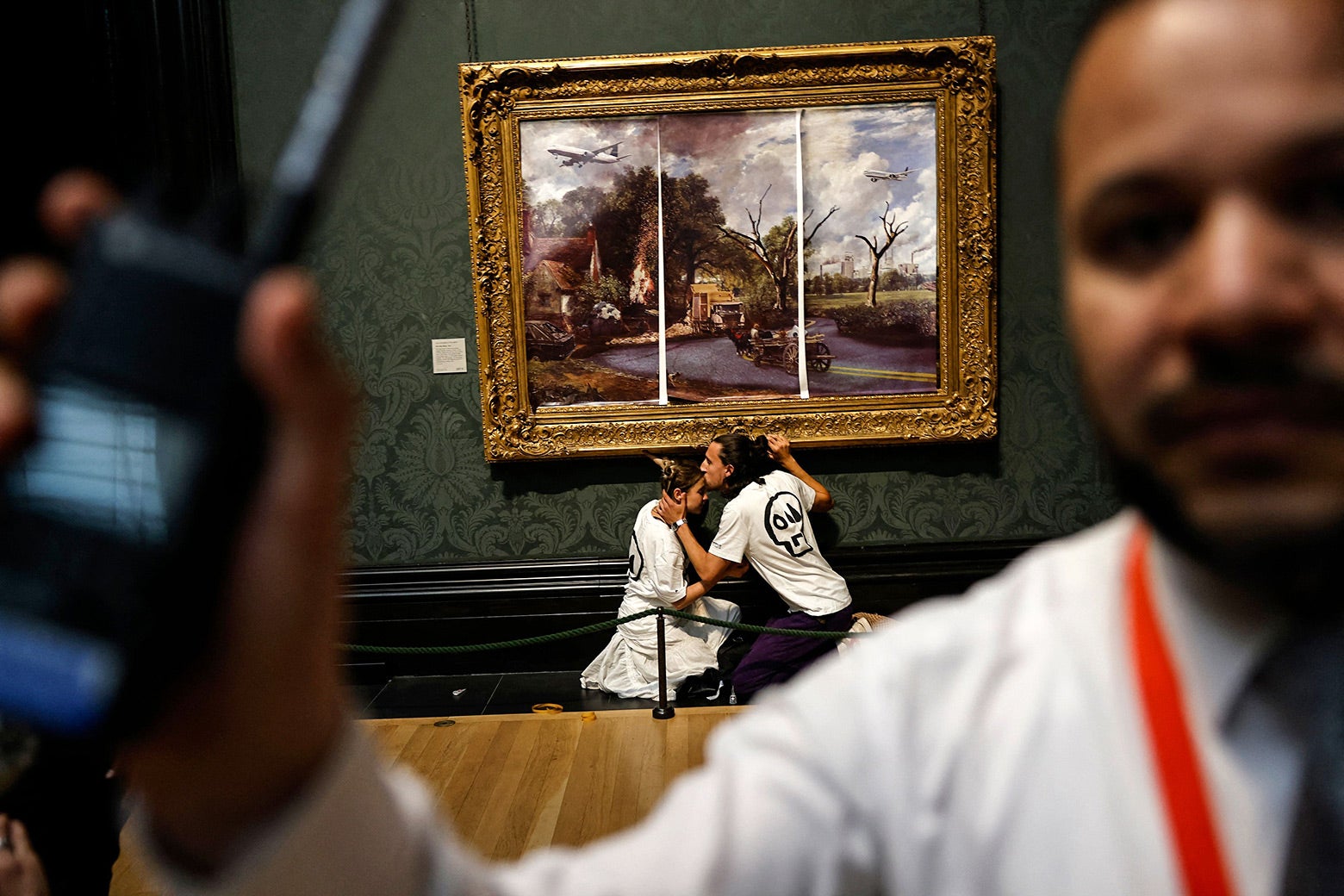 Activists from the 'Just Stop Oil' campaign group, with hands glued to the frame of the painting 'The Hay Wain' by English artist John Constable. A security guard tries to block the photo.