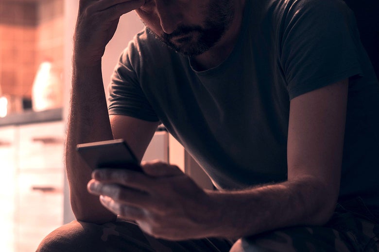 A man looks down at his phone in his hand with his other hand on his forehead.