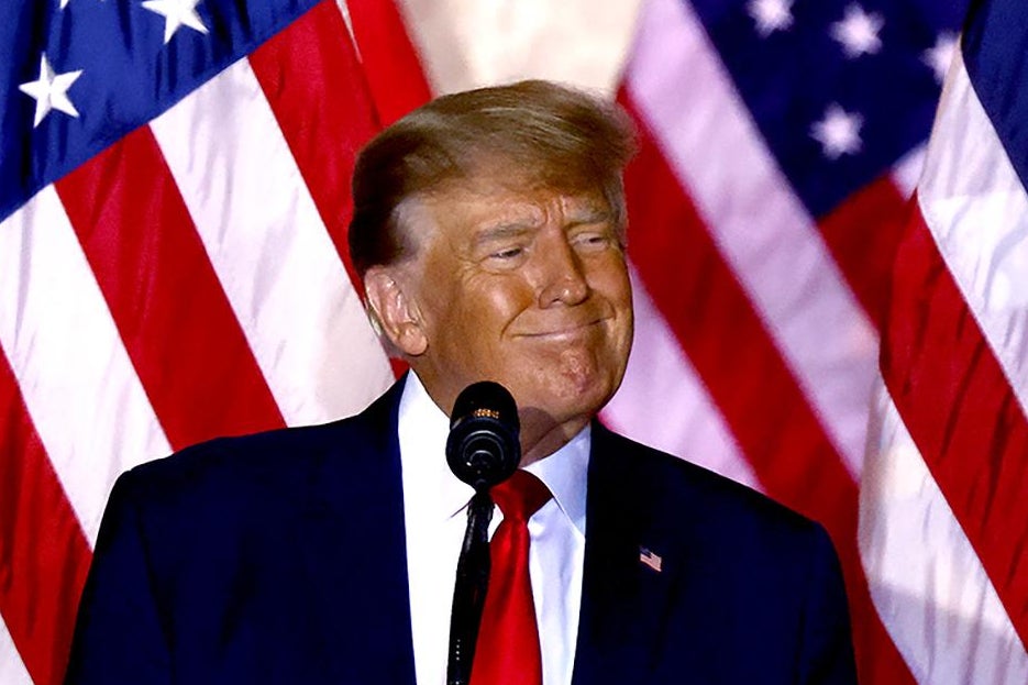 Trump smirks at the microphone with USA flags behind him