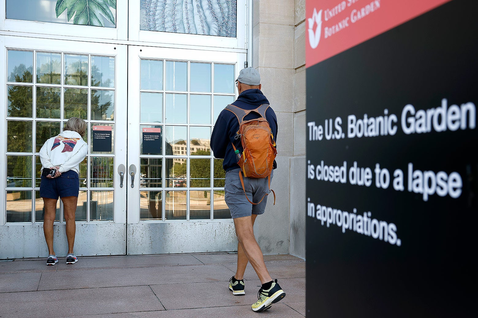 Twee mensen gluren door de deuren van de U.S. Botanic Garden, die gesloten is vanwege een tekort aan financiële middelen.