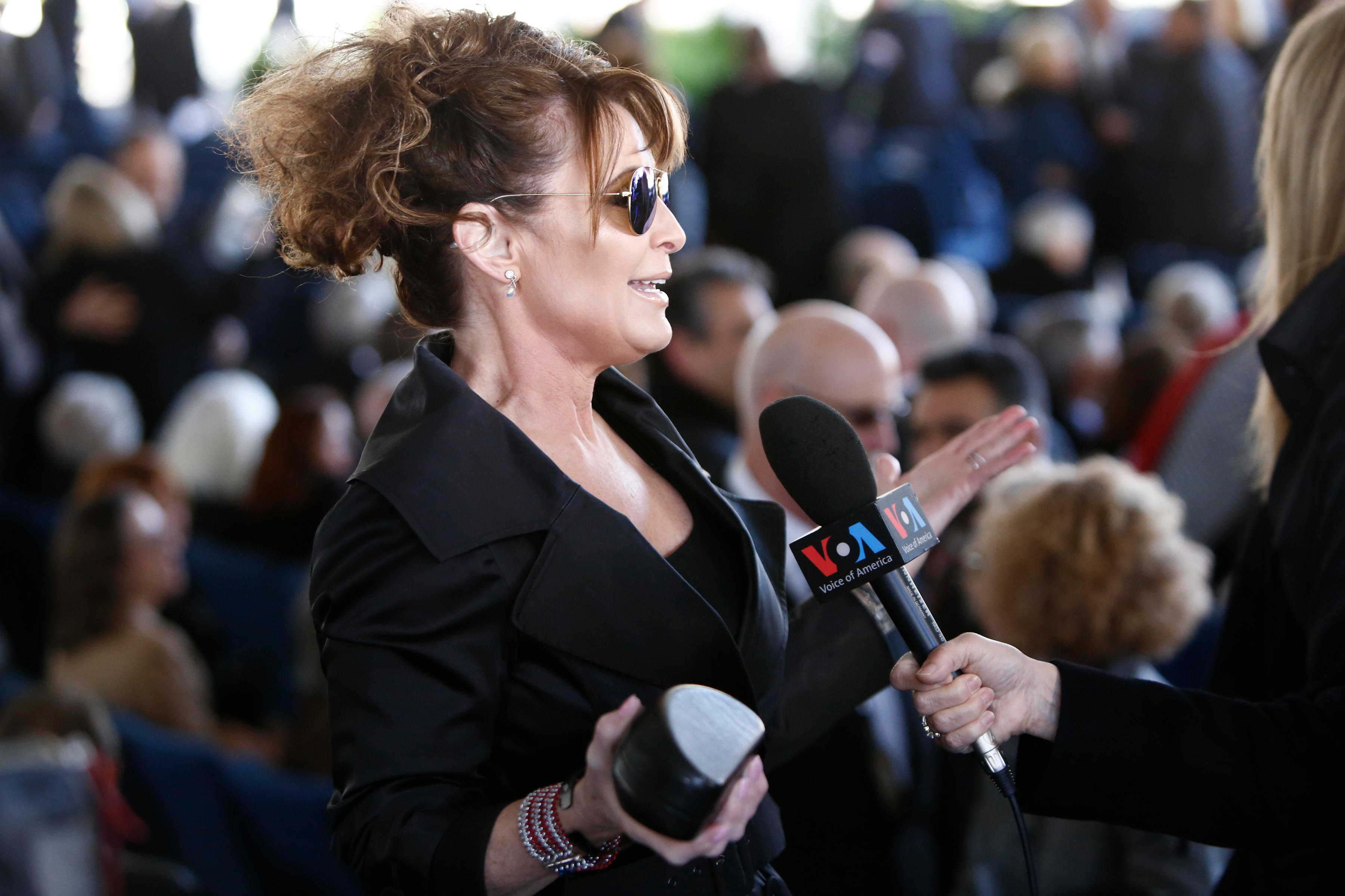 Sarah Palin, wearing black, talks to a Voice of America reporter at Billy Graham's funeral.