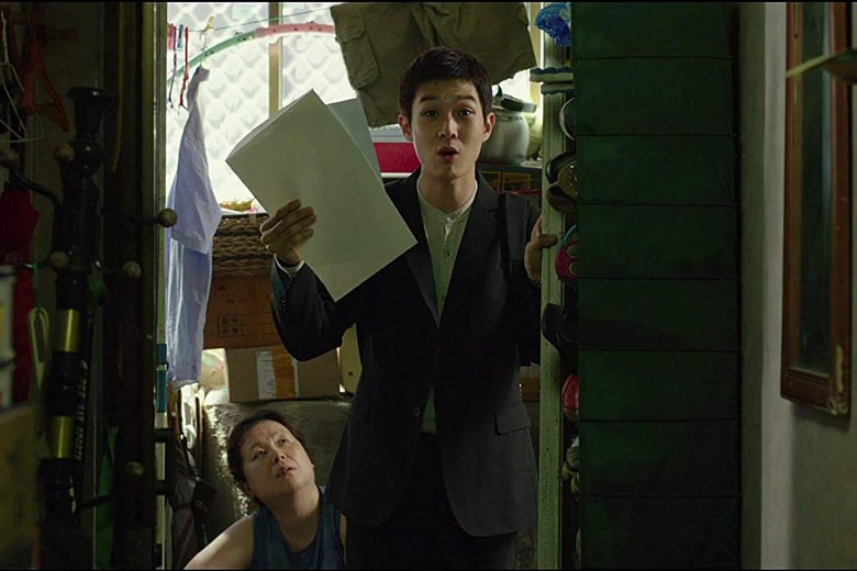 A still from Parasite showing actor Choi Woo-shik holding up two sheets of paper excitedly.
