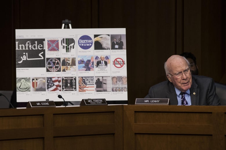 Sen. Patrick Leahy sits in a committee room next to a poster board showing several examples of Russian-created Facebook pages. 