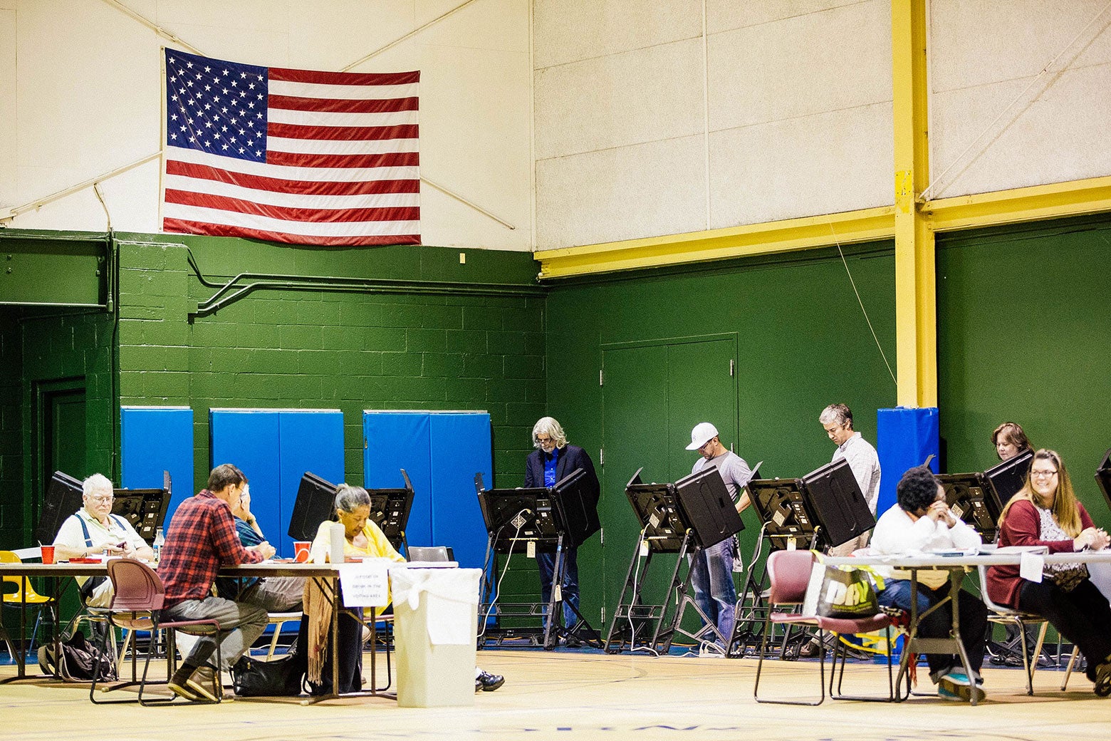 Voters stand behind electronic machines in a rec center gym.