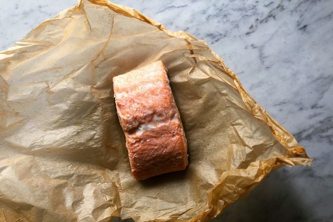 Piece of cooked salmon on brown wax paper on a marble countertop.