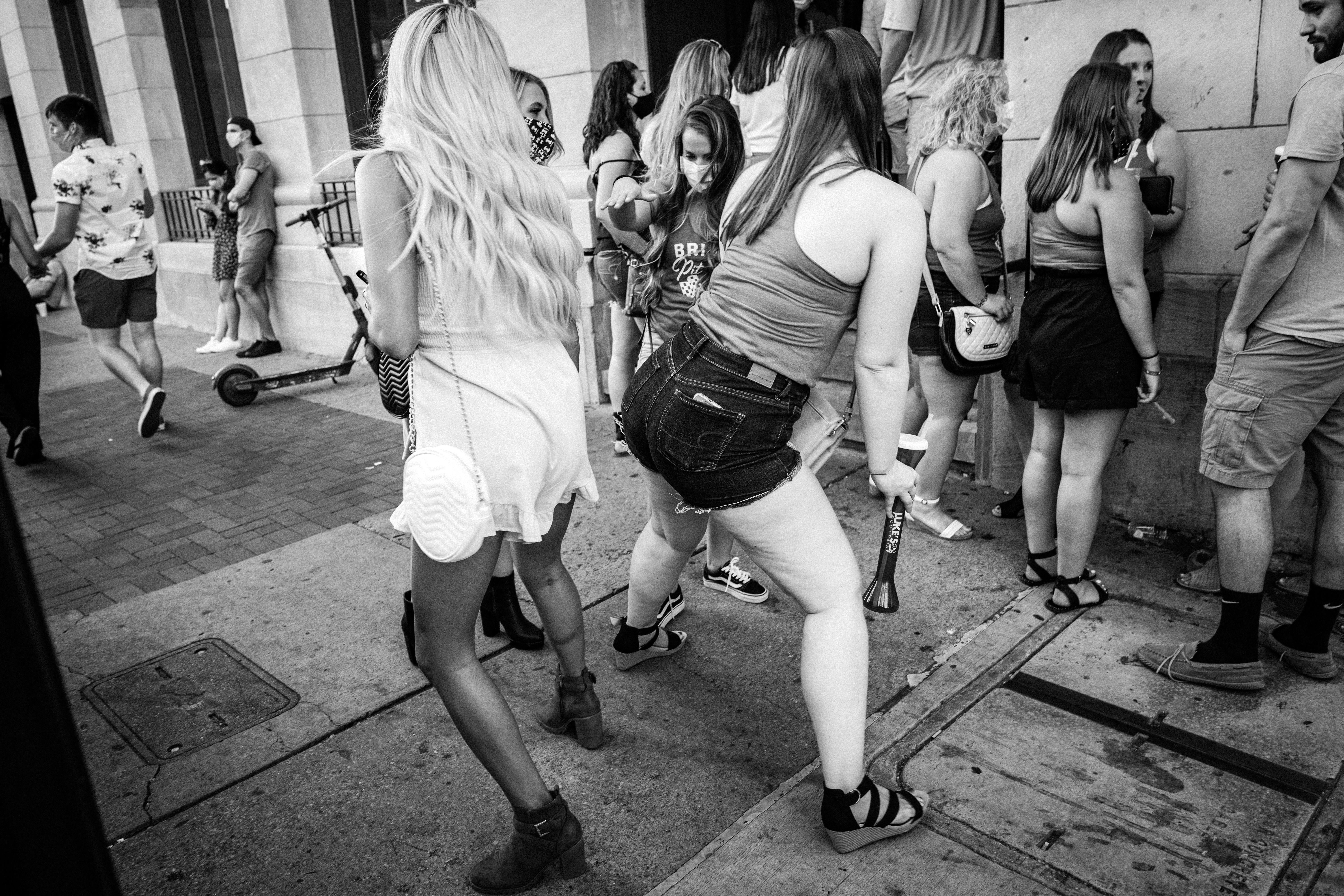 A black-and-white photo shows women holding drinks dancing together on the sidewalk.