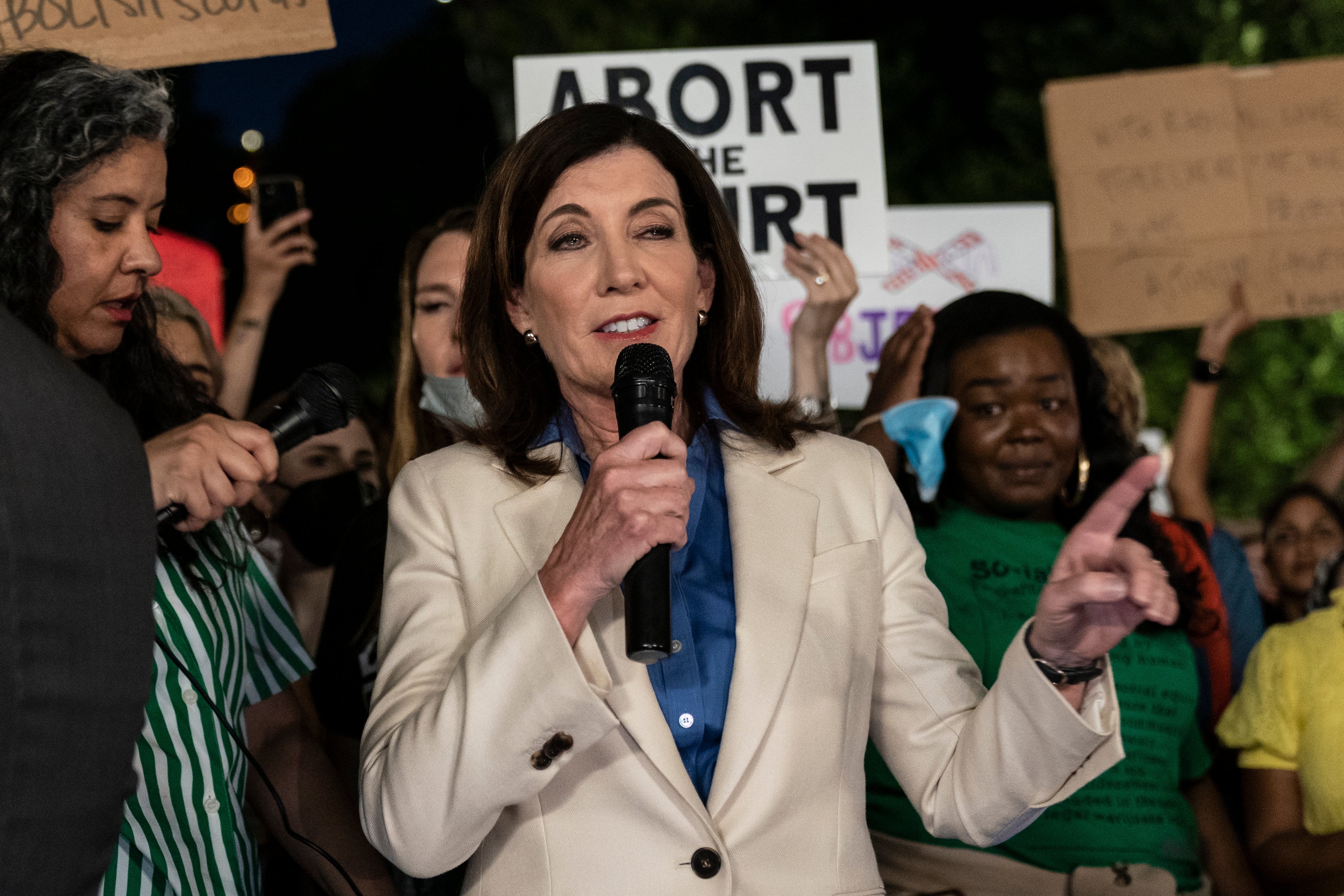 A woman stands in front of protesters who are are holding signs that read "Abort the Court."