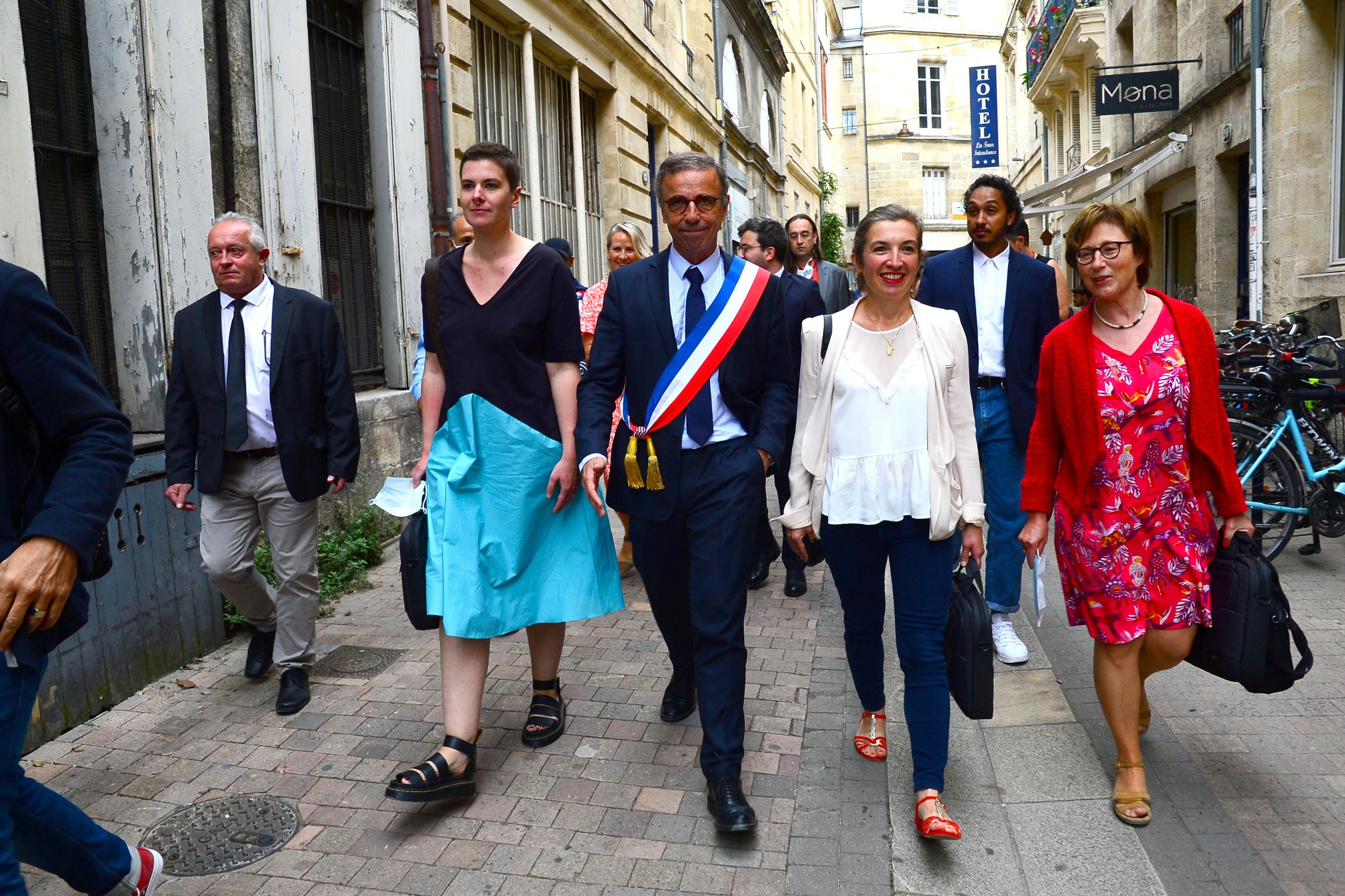The new mayor of Bordeaux, wearing a sash, walks down the street flanked by advisers.