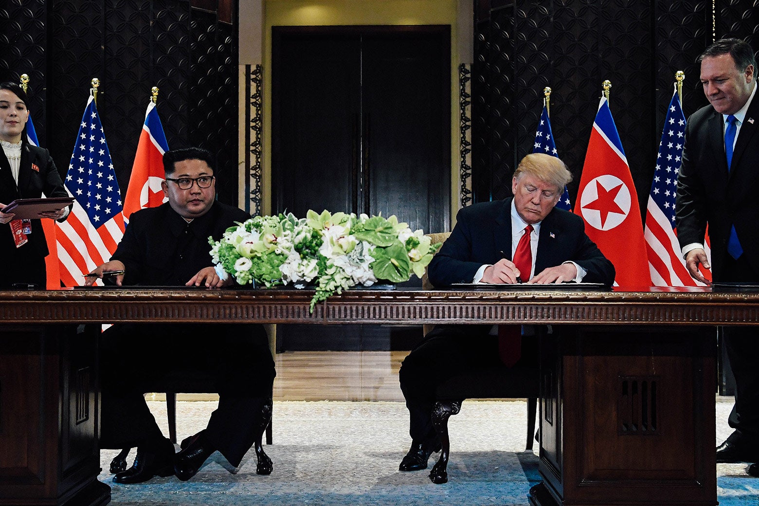 Kim Jong-un and Donald Trump seated at a large desk, signing documents.
