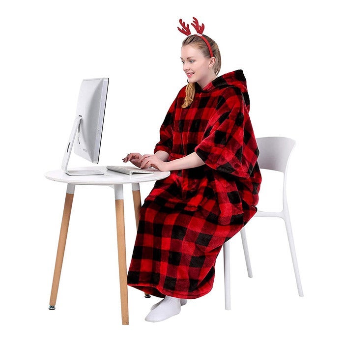 A woman at a computer in a wearable blanket and a festive antler headband.