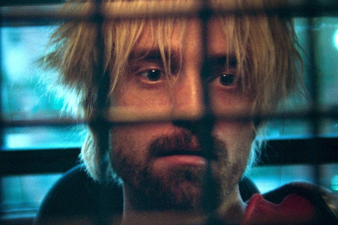 Robert Pattison, with blonde hair, stares from behind a grate.