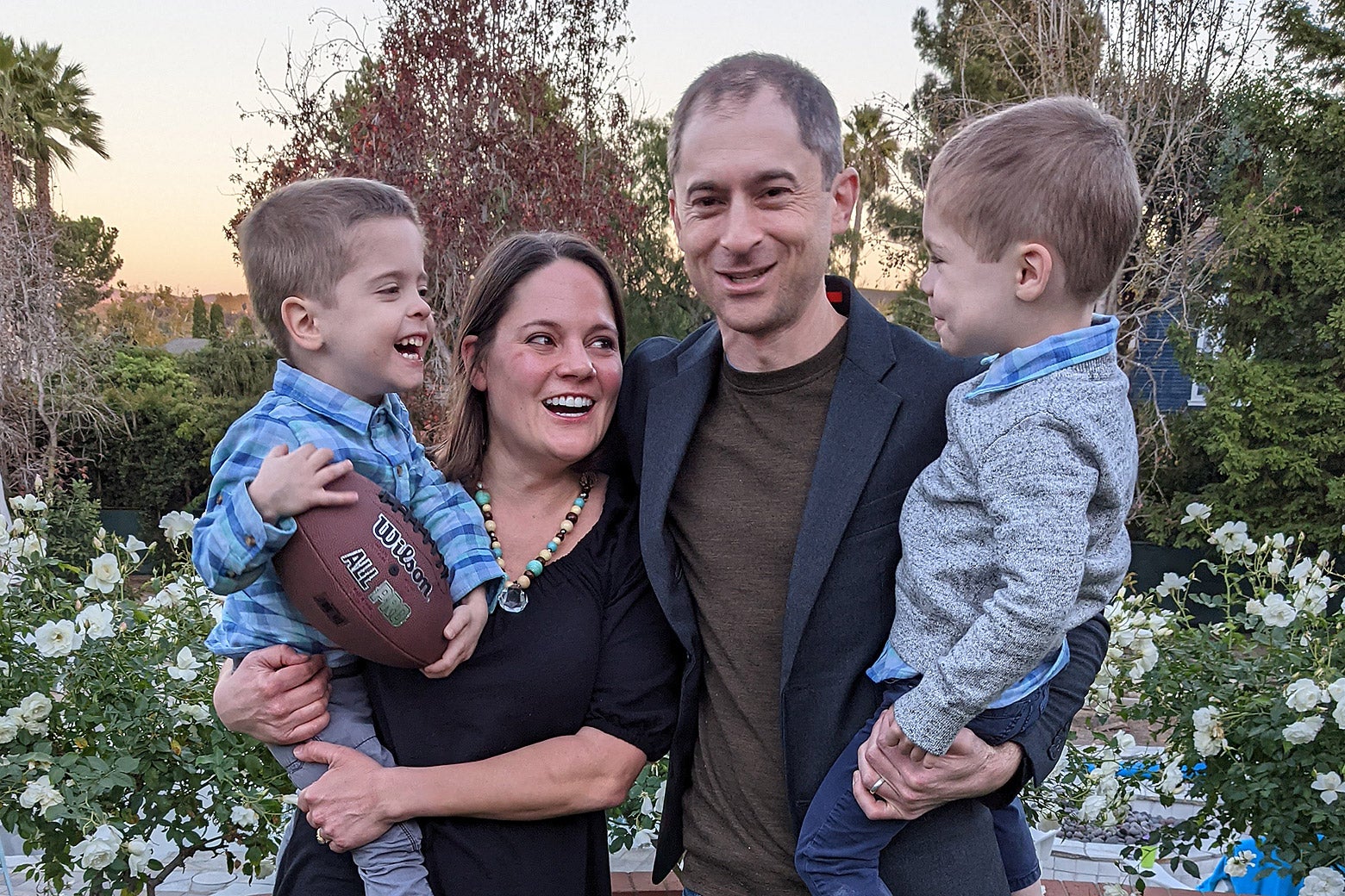 A man and a woman each hold one toddler boy in a family photo against a backdrop of spring flowers.