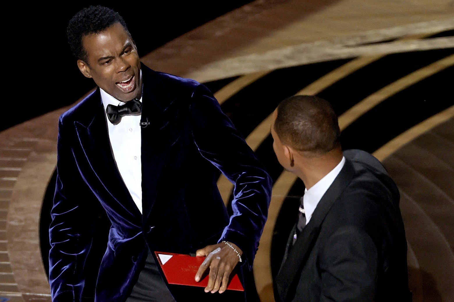 Chris Rock open-mouthed and reeling back in shock as Will Smith stands in front of him on the Oscars stage