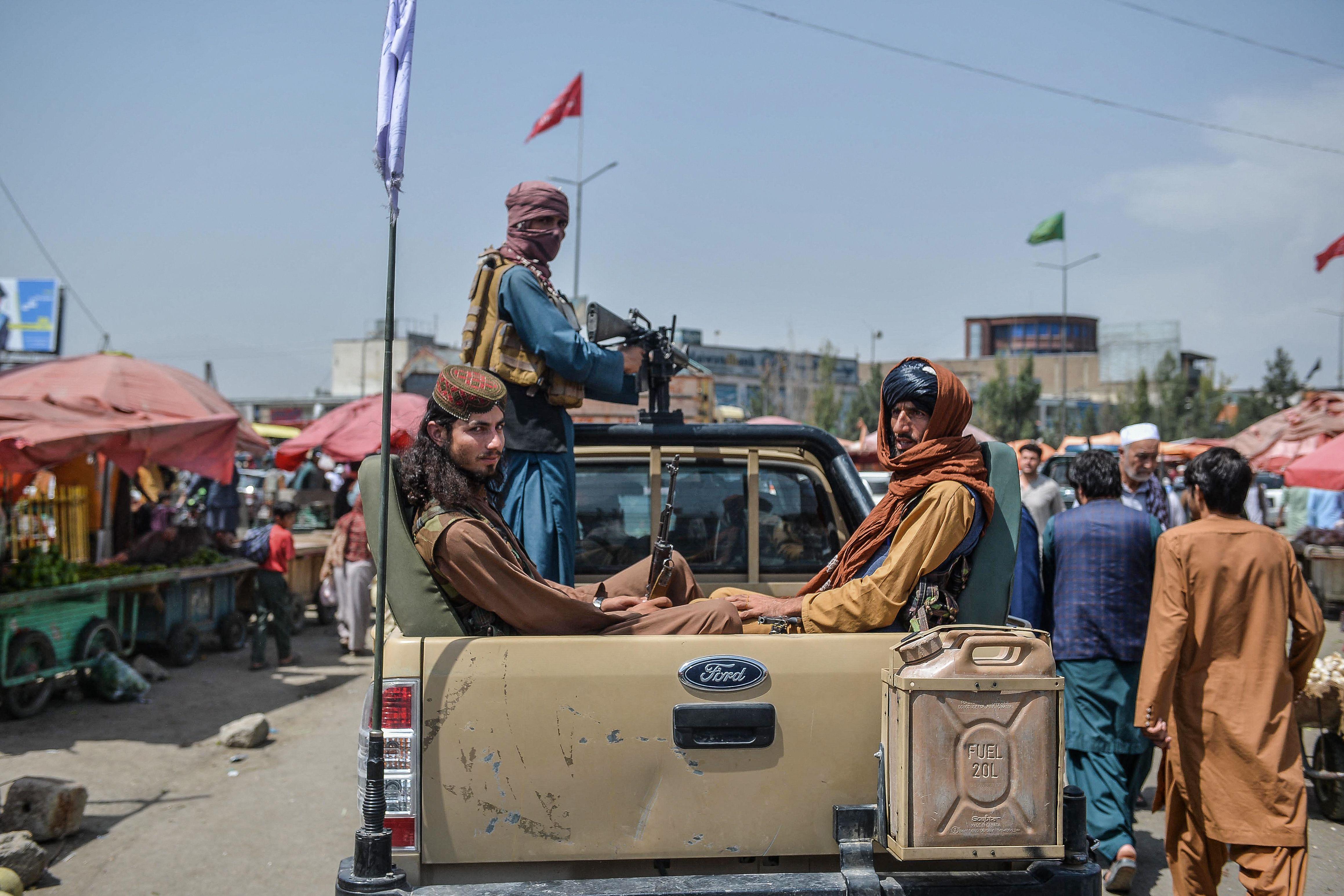 Taliban fighters ride in the back of a pickup truck through a crowded market area