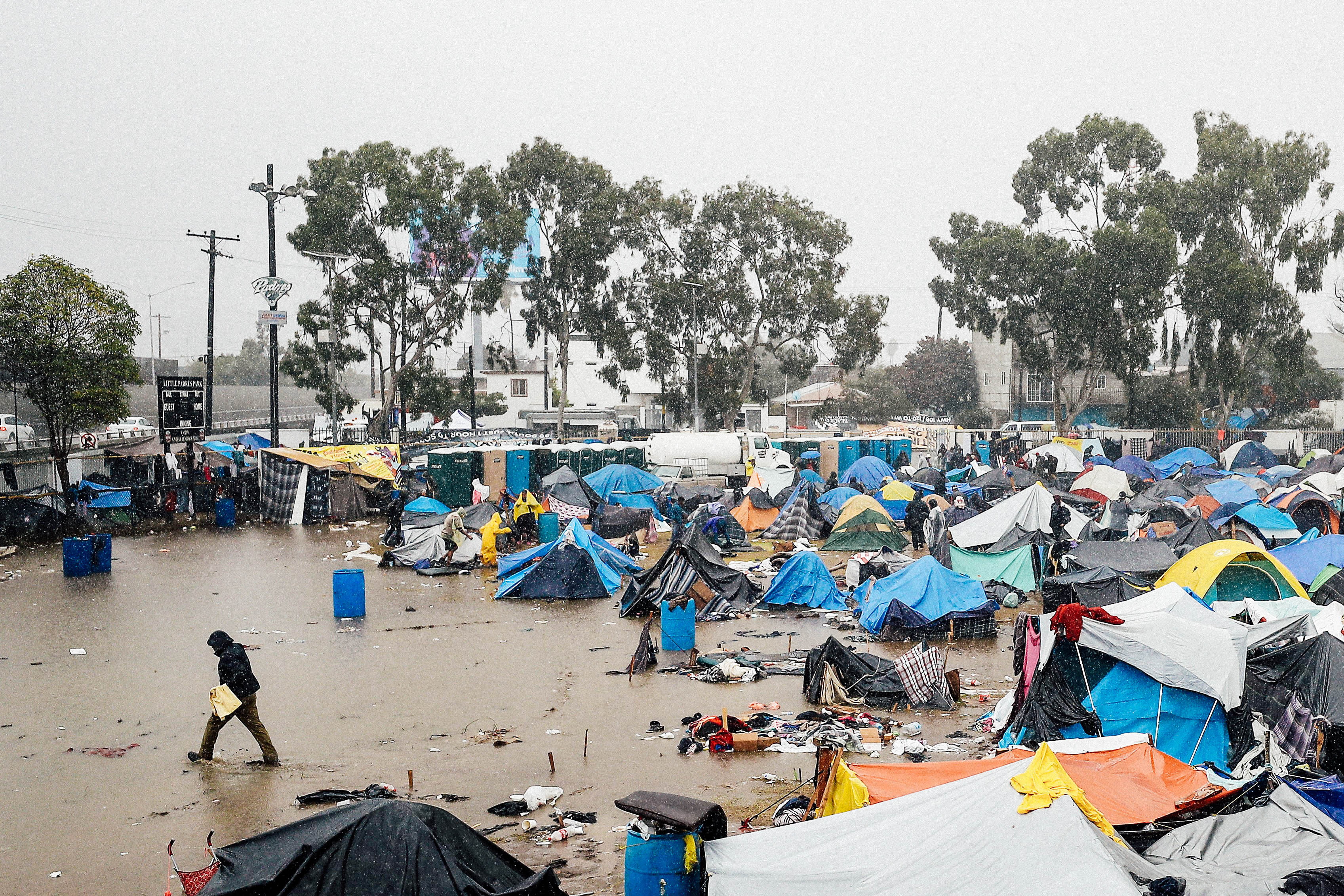 A person walks through a tent encampment flooded by rain.