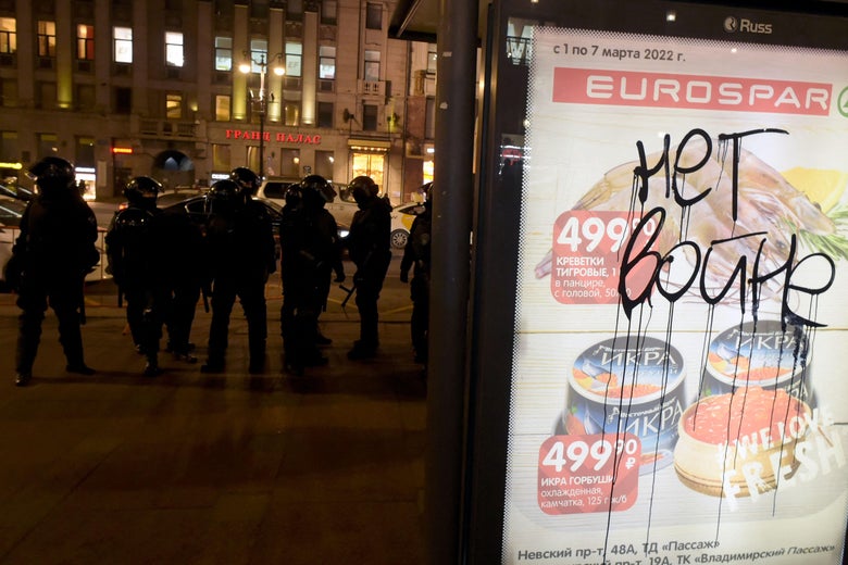 Russian letters scrawled on an advertisement in front of riot police officers at night.