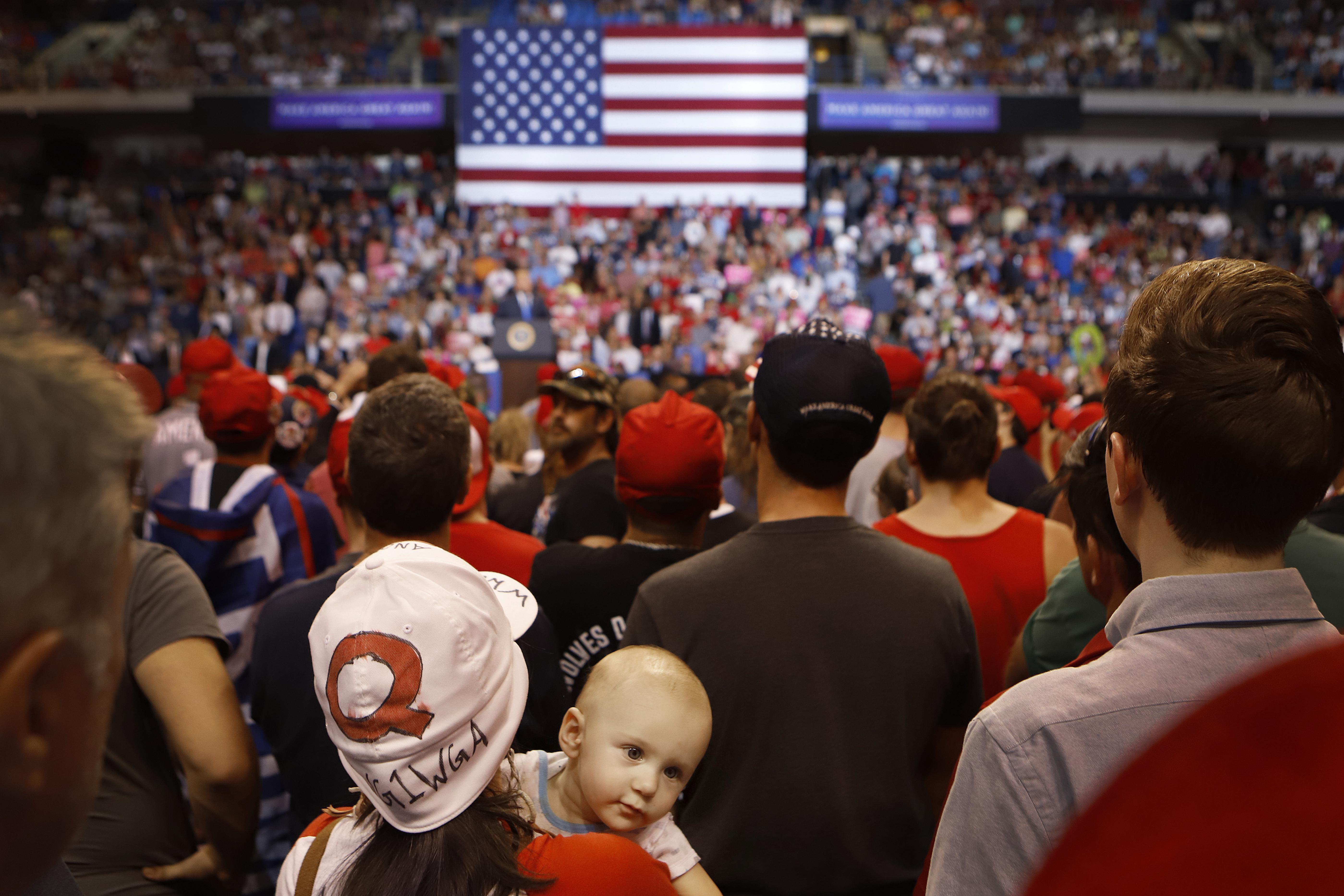 Roxanne Kravitz, wearing a 'Q' hat with her son Indigo, listen to President Donald J. Trump speak to a large crowd on August 2, 2018 at the Mohegan Sun Arena at Casey Plaza in Wilkes Barre, Pennsylvania. 'Q' represents QAnon, a conspiracy theory group that has been seen at recent rallies.  (Photo by Rick Loomis/Getty Images)