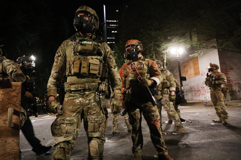 Cops in riot gear stand near a building.
