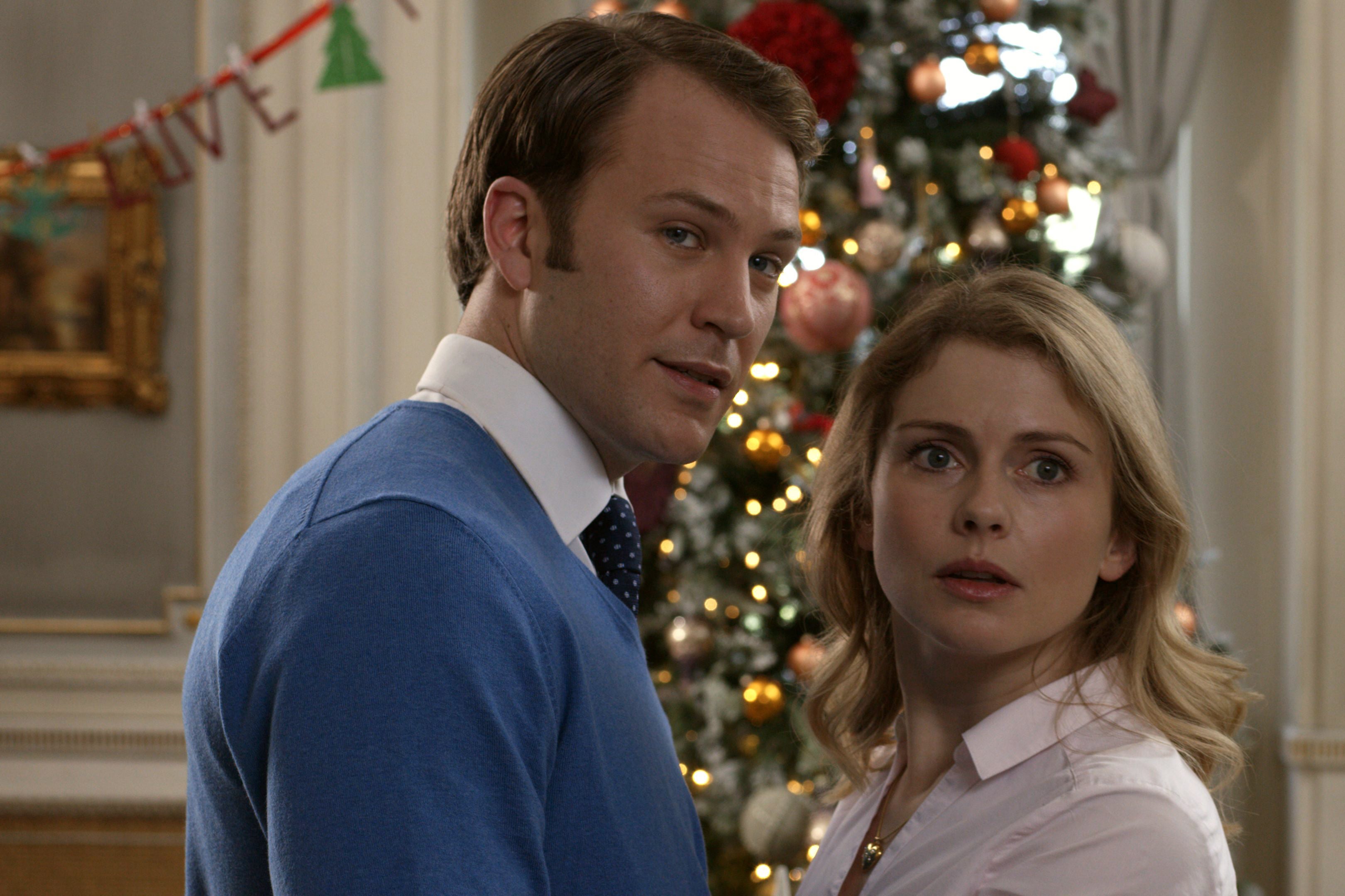 Ben Lamb and Rose McIver in a production still from the Netflix movie A Christmas Prince: The Royal Wedding. They stand facing each other in front of a Christmas tree.