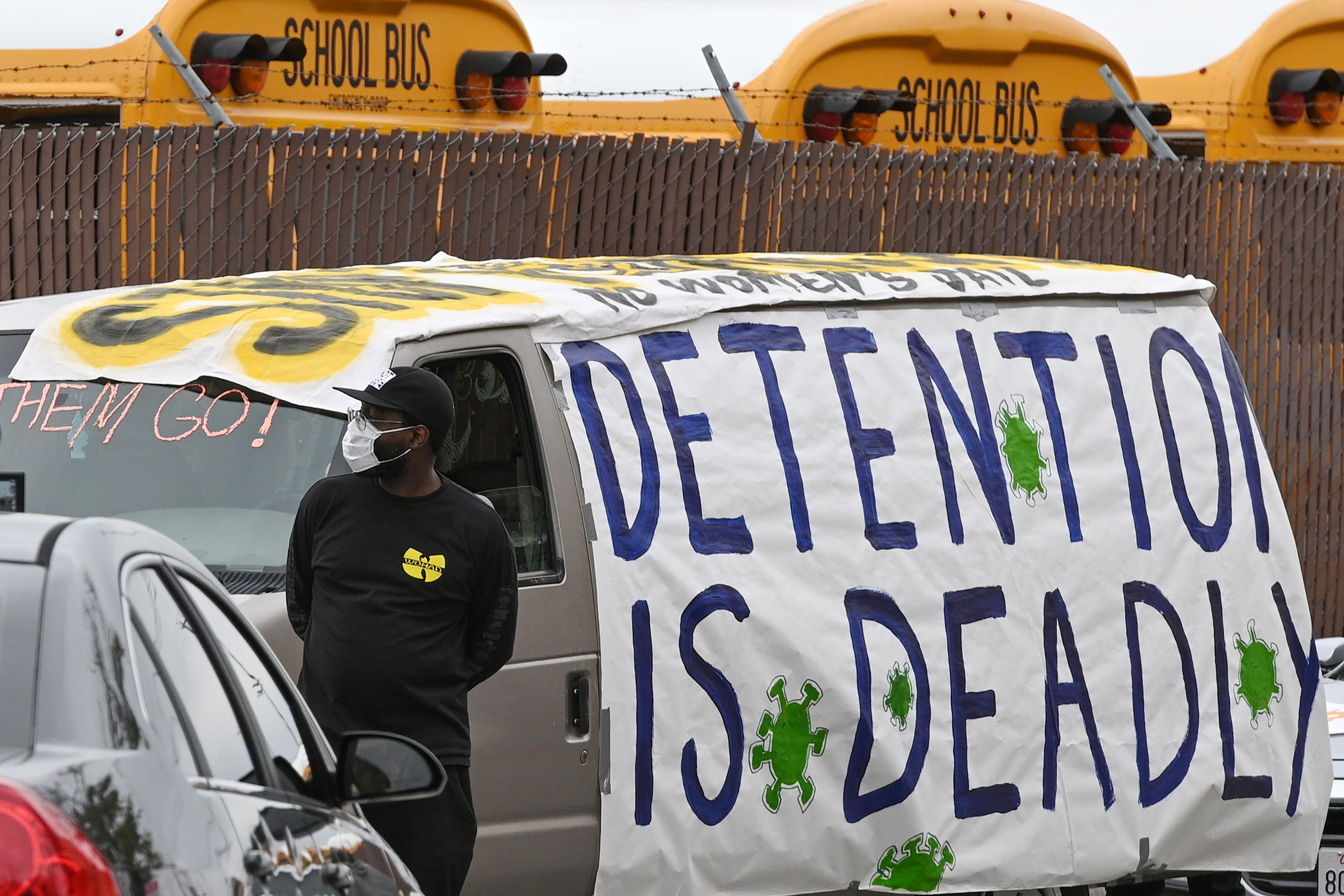 A protester stands by a van marked with the sign "detention is deadly."