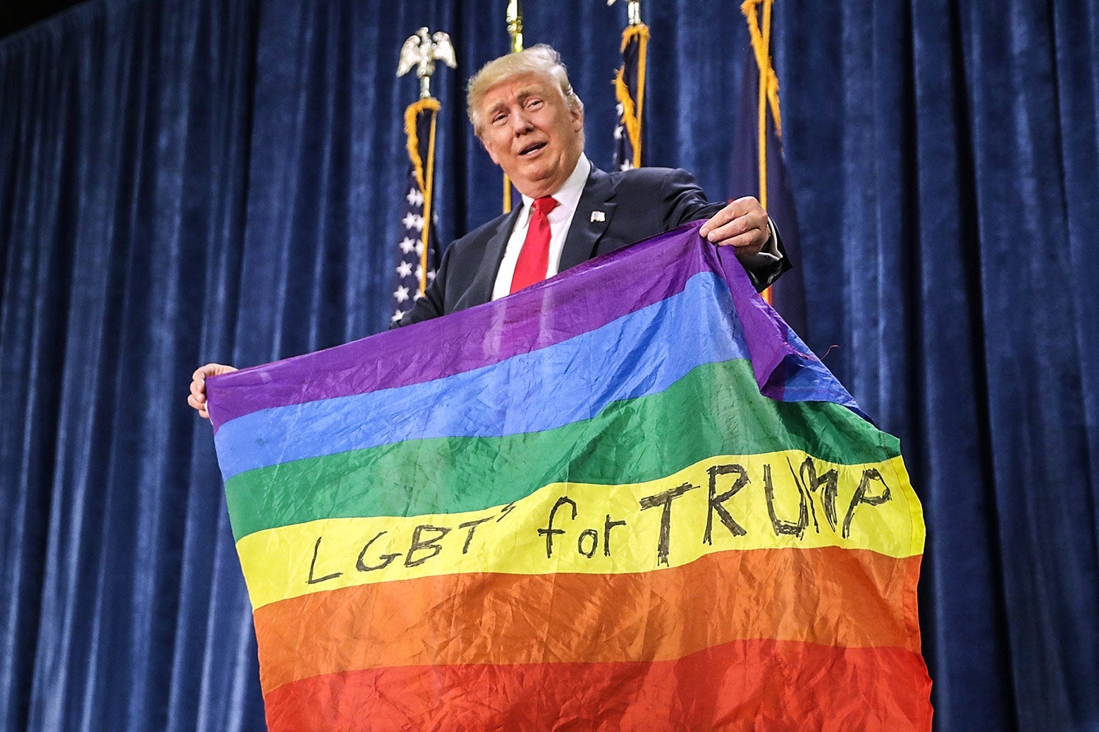 Donald Trump holds up a rainbow flag with the words "LGBTs for Trump" handwritten in the yellow stripe.