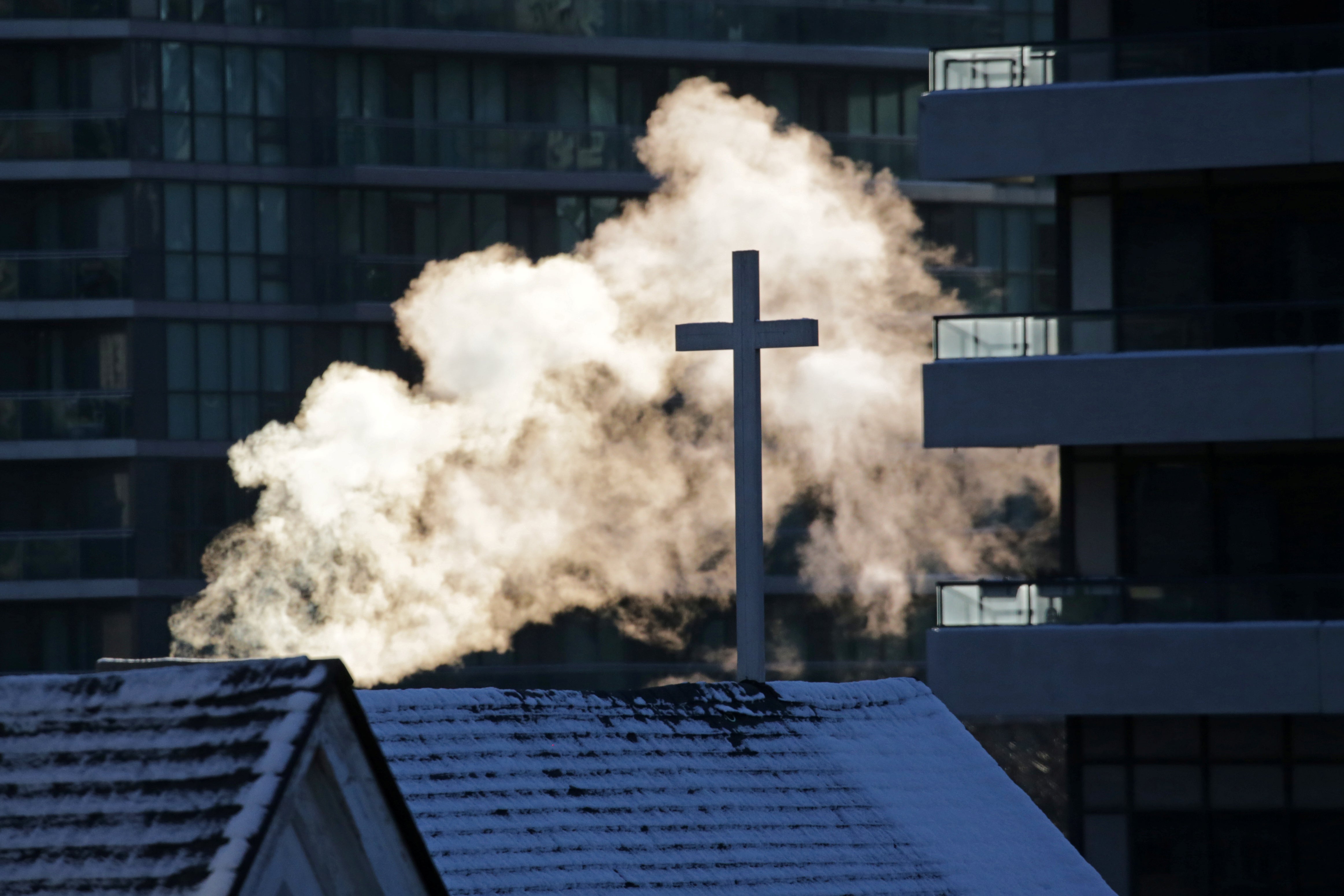 Steam rises behind a cross atop a church.