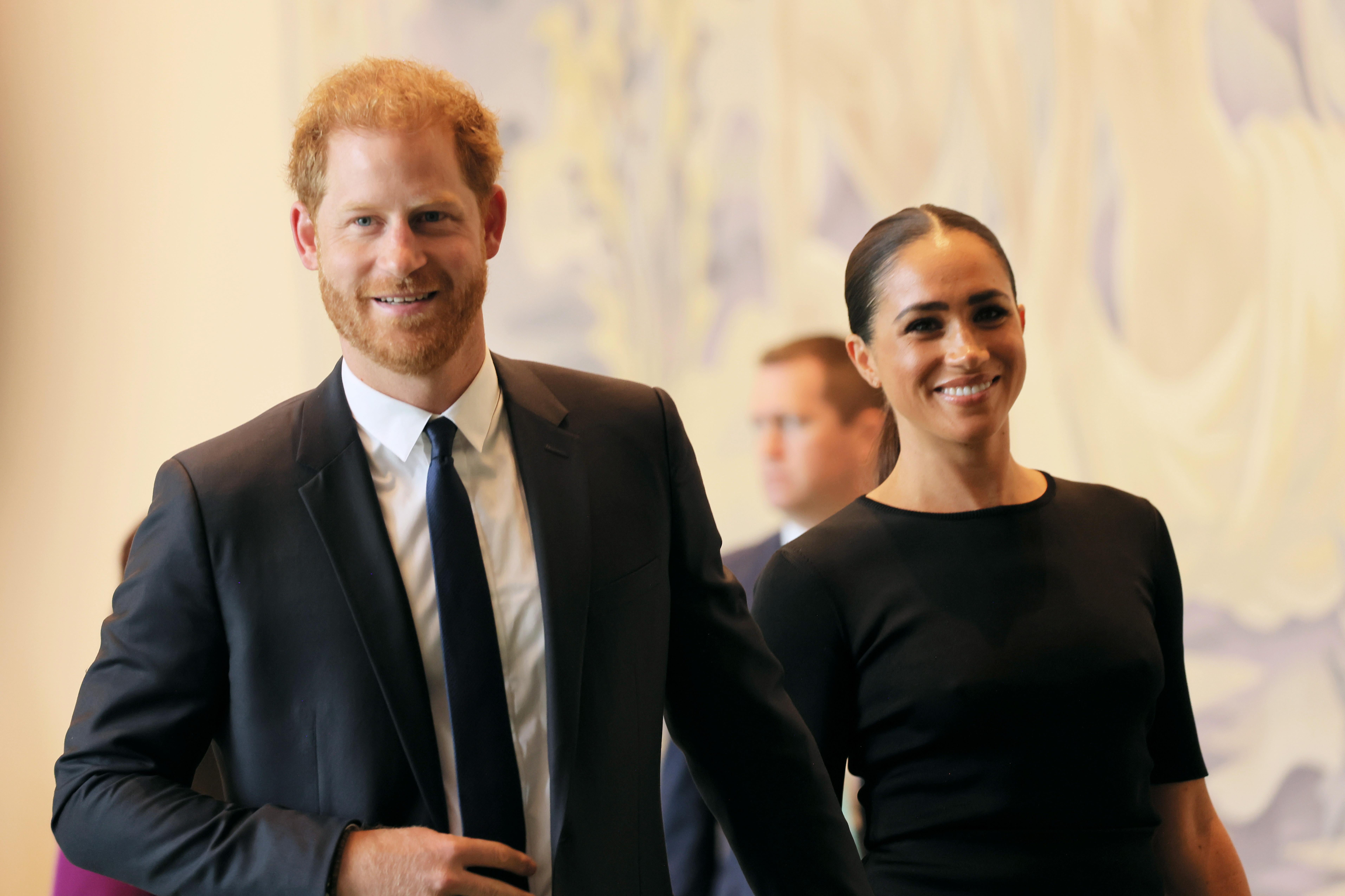 Harry and Meghan hold hands and smile.