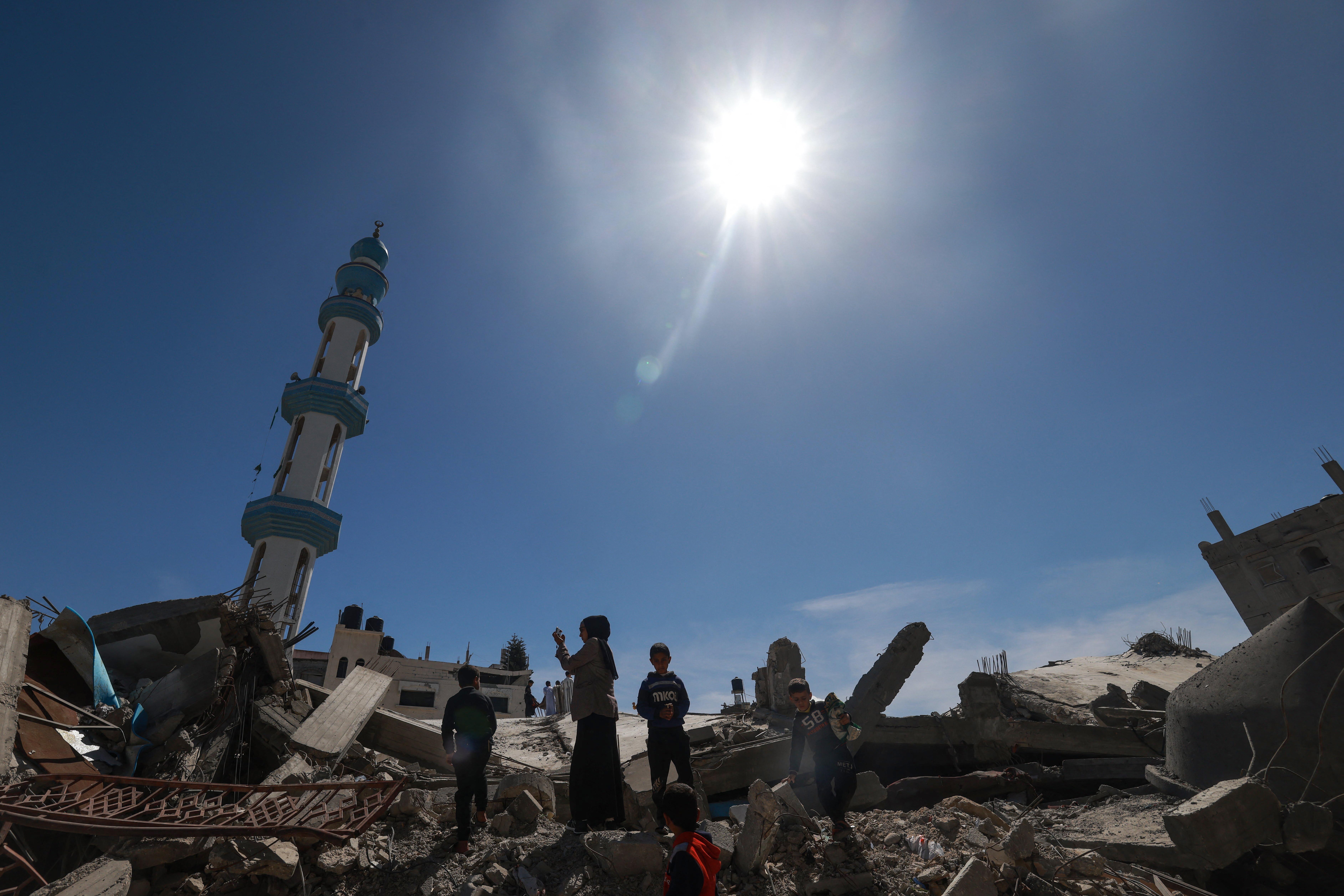A woman and several children walk over rubble with a minaret in the background.
