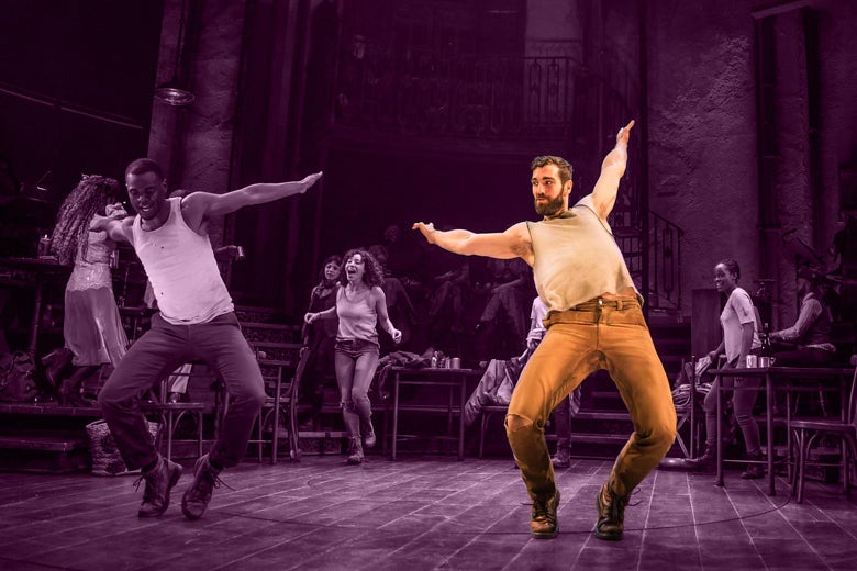 Two men wearing white tank tops dance with arms outstretched at the front of the stage, with other actors in the background. Hughes is on the right, highlighted.