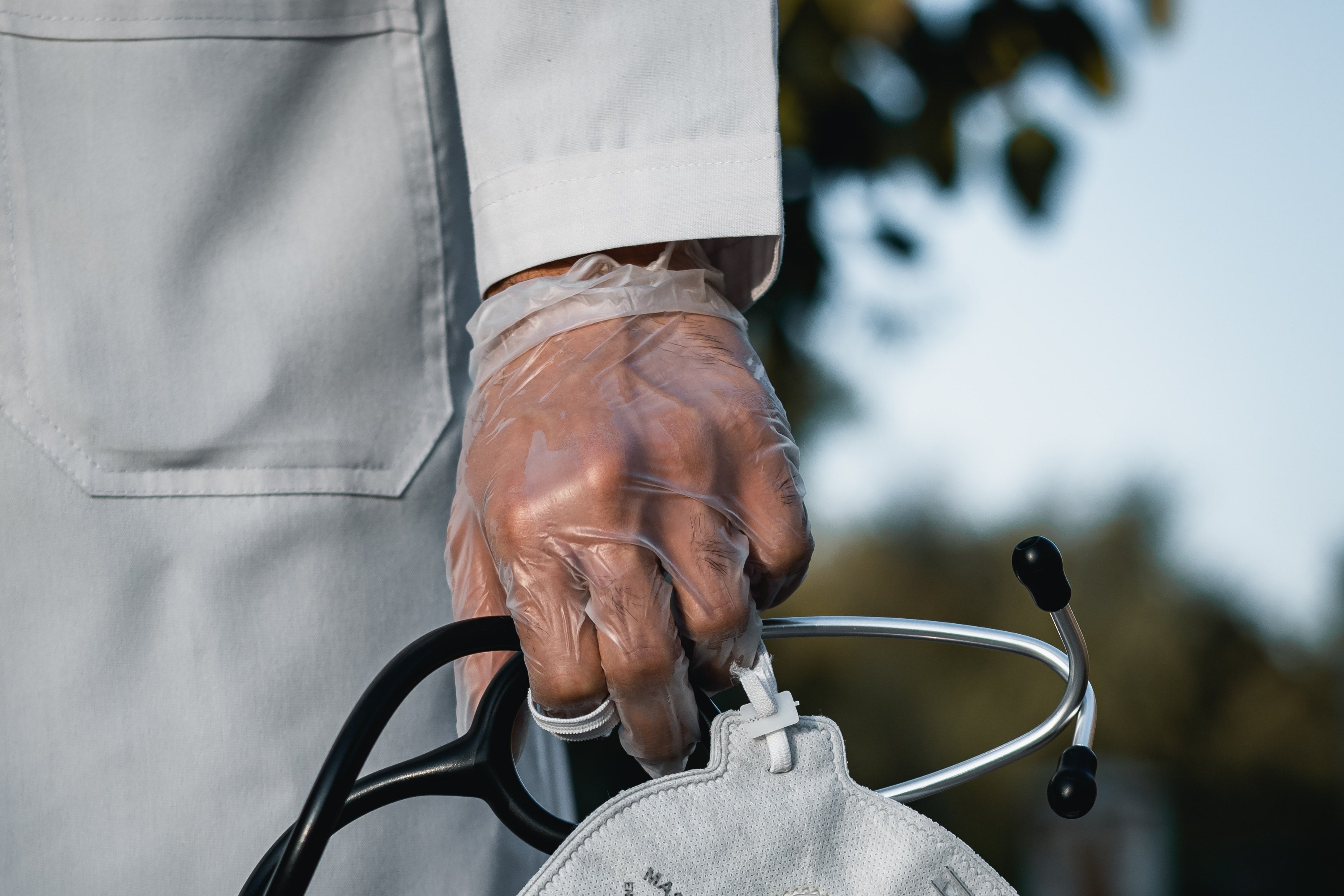 A gloved hand holds a stethoscope and mask