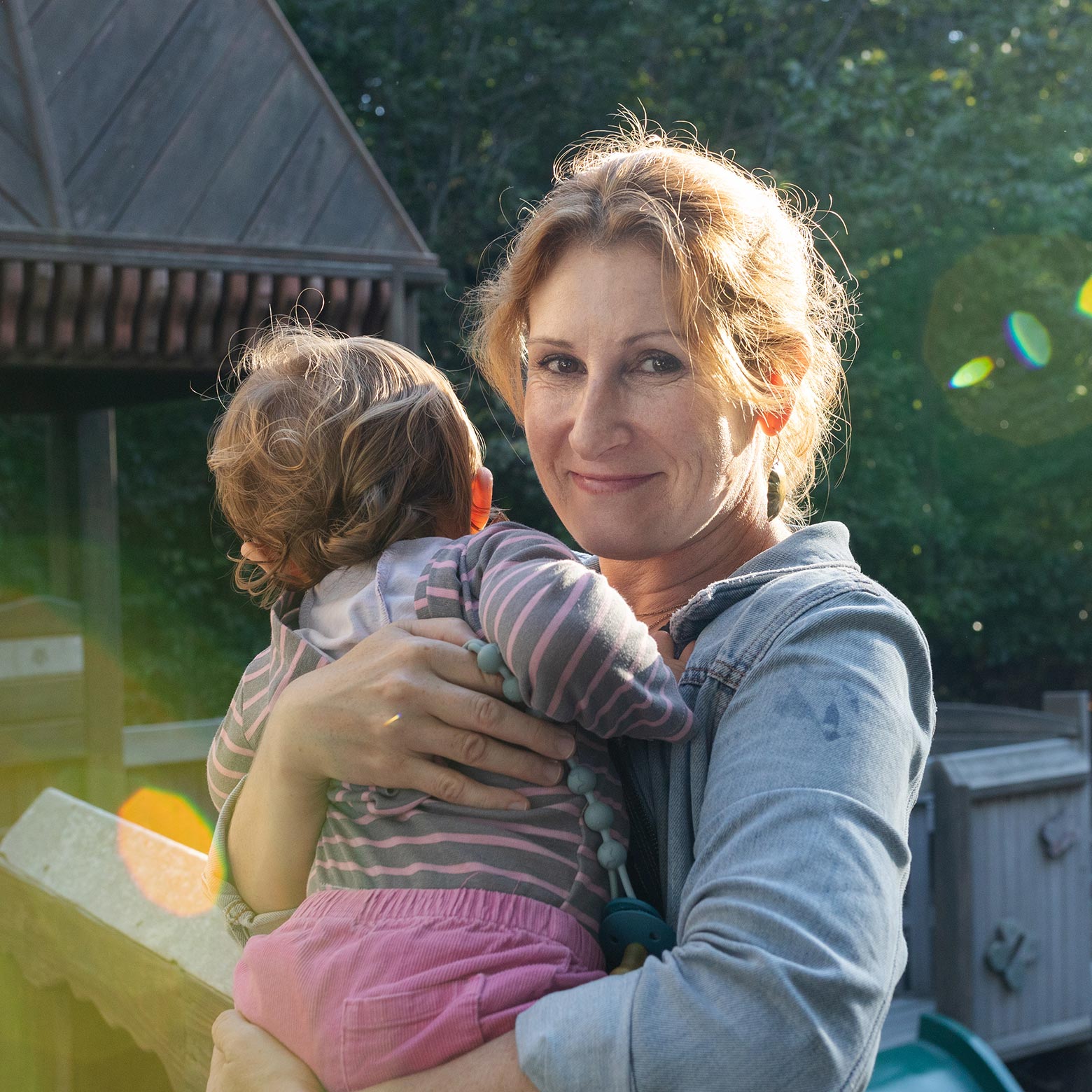 A mother holding a toddler outdoors.
