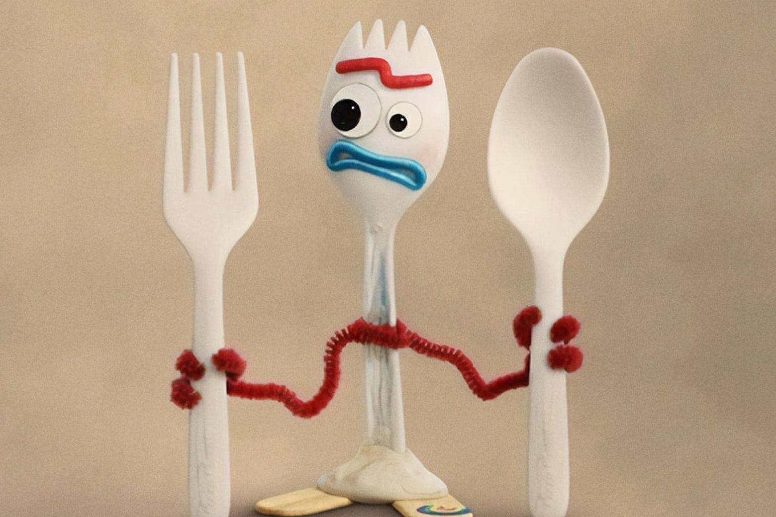 Forky, a toy made from a spork with pipe cleaner arms, holding a plastic fork in one hand and a plastic spoon in the other, looking disgusted.