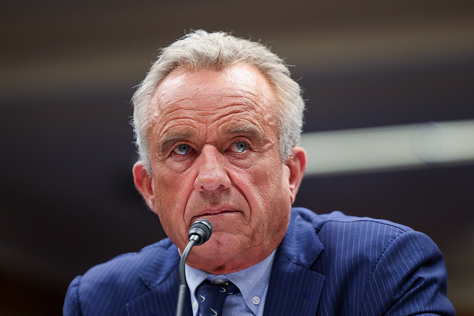 RFK Jr. sitting at a desk positioned in front of a small microphone.