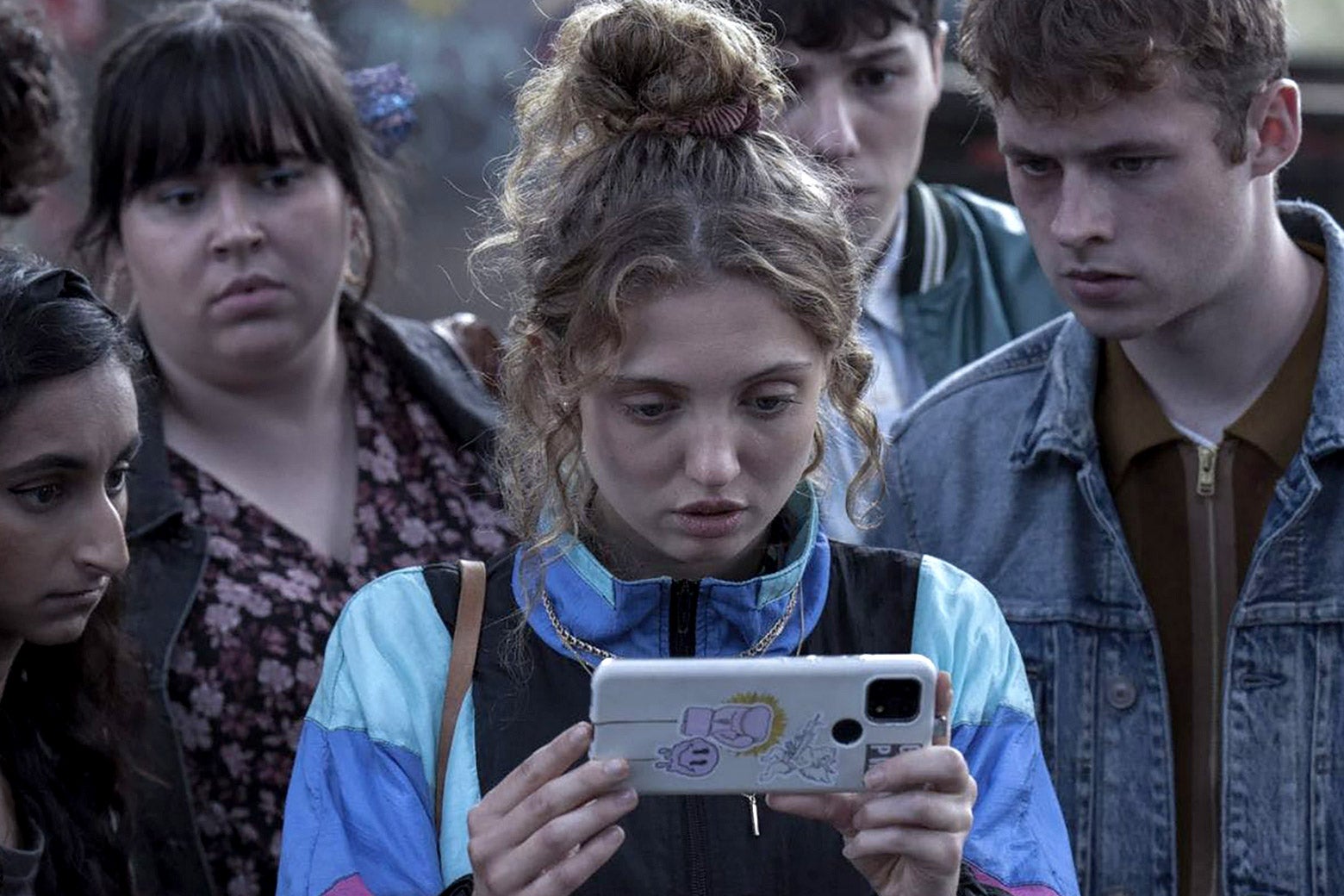 A teen looks shocked holding her smartphone in a crowd.