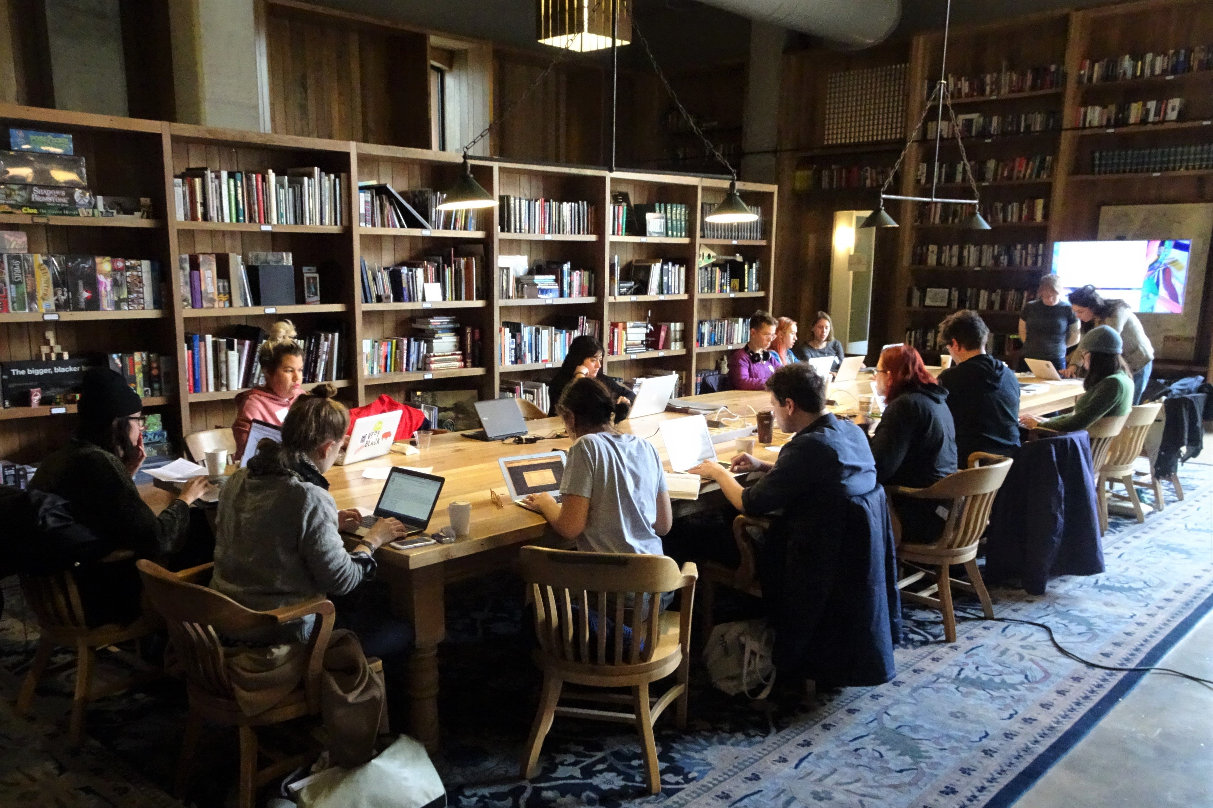 People working on laptops at a long communal table in the Kickstarter library.
