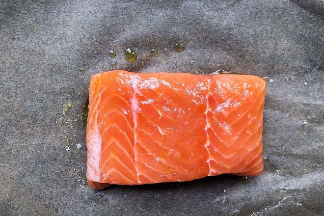 A piece of raw salmon, drizzled with oil and sprinkled with salt, on a piece of wax paper.