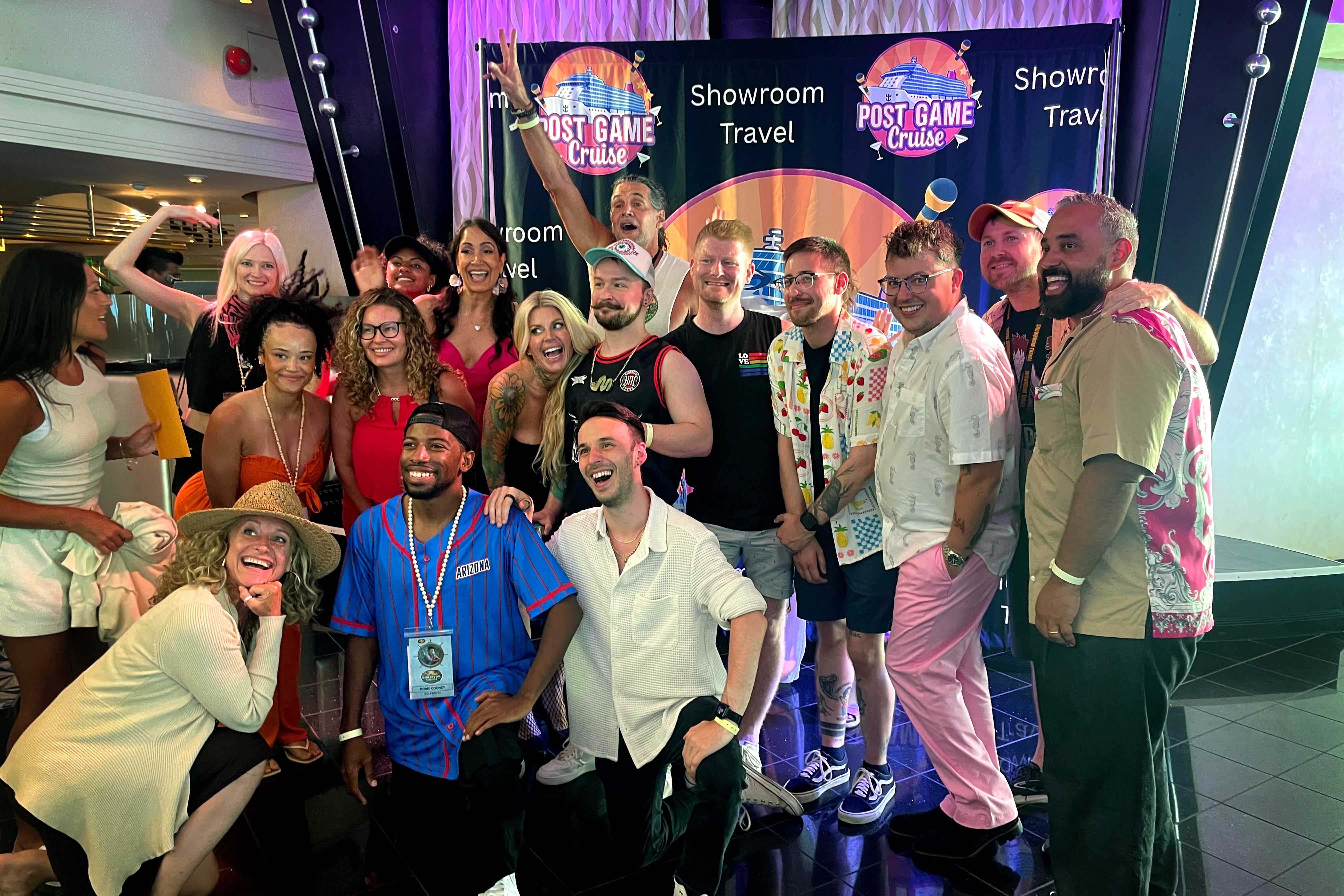 The 14 previous Survivor contestants posing on board the ship, in front of a Survivor-logo backdrop.