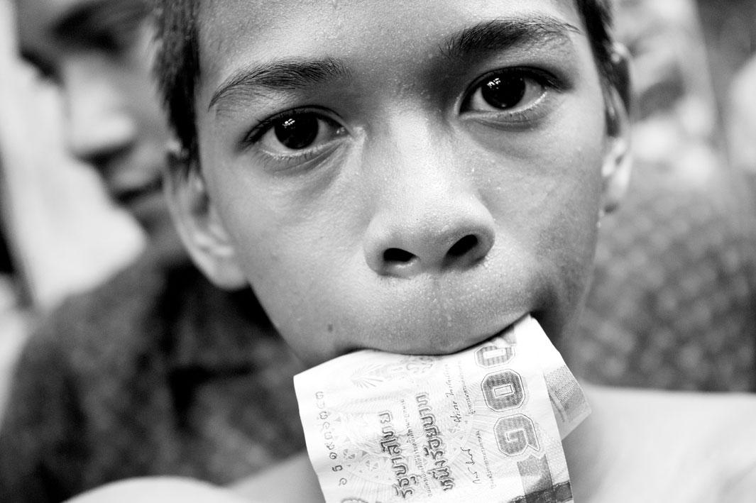 A boy with money in his mouth. After winning the boxing match winner goes around and collects money from tourists certificates. After that, the money is divided, the coach gets the largest share.