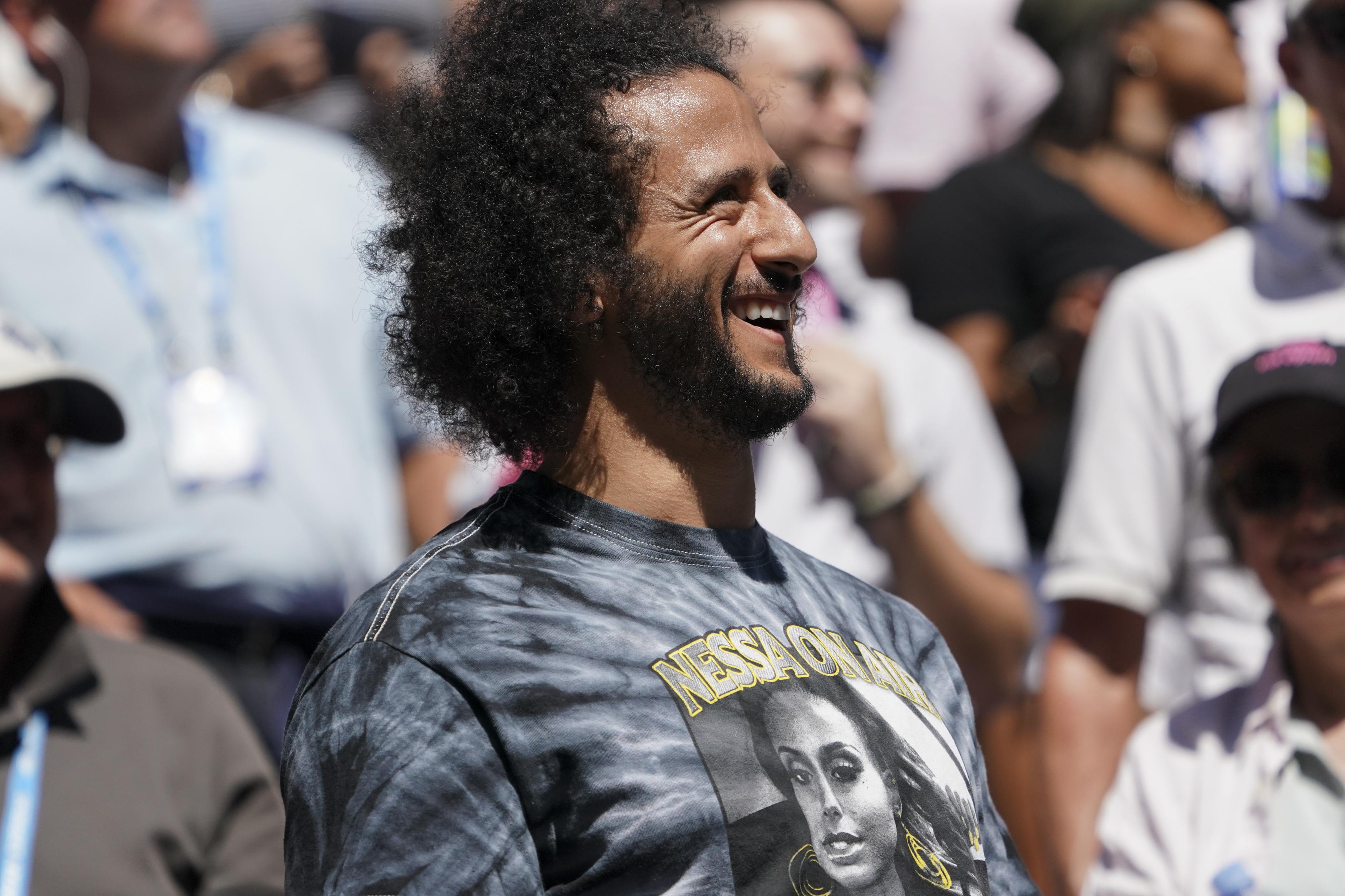 Colin Kaepernick smiles while in the stands at a tennis match.